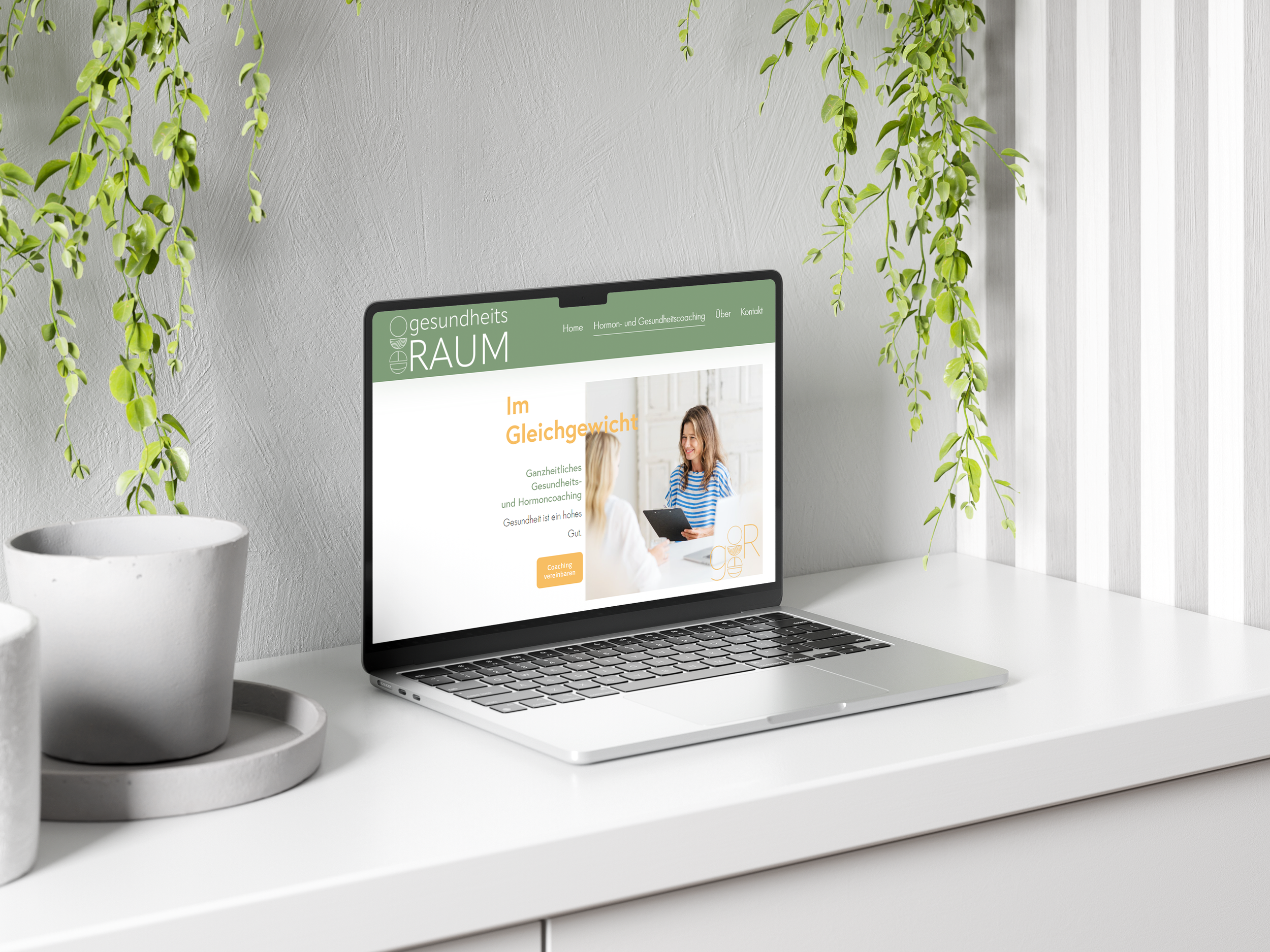 Ein MacBook auf einem weißen Tisch mit einem Website-Design, das eine Beratung zum Thema Hormon- und Gesundheitcoaching zeigt, umgeben von Weißtöpfen und grünen Pflanzen, in einem hellen Raum mit vertikalen weißen Fensterläden.