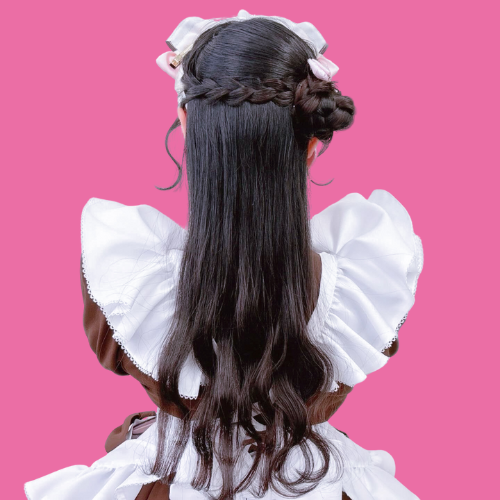 A girl with long, dark hair styled in braids and loose waves, wearing a white dress with puffy sleeves, against a pink background.