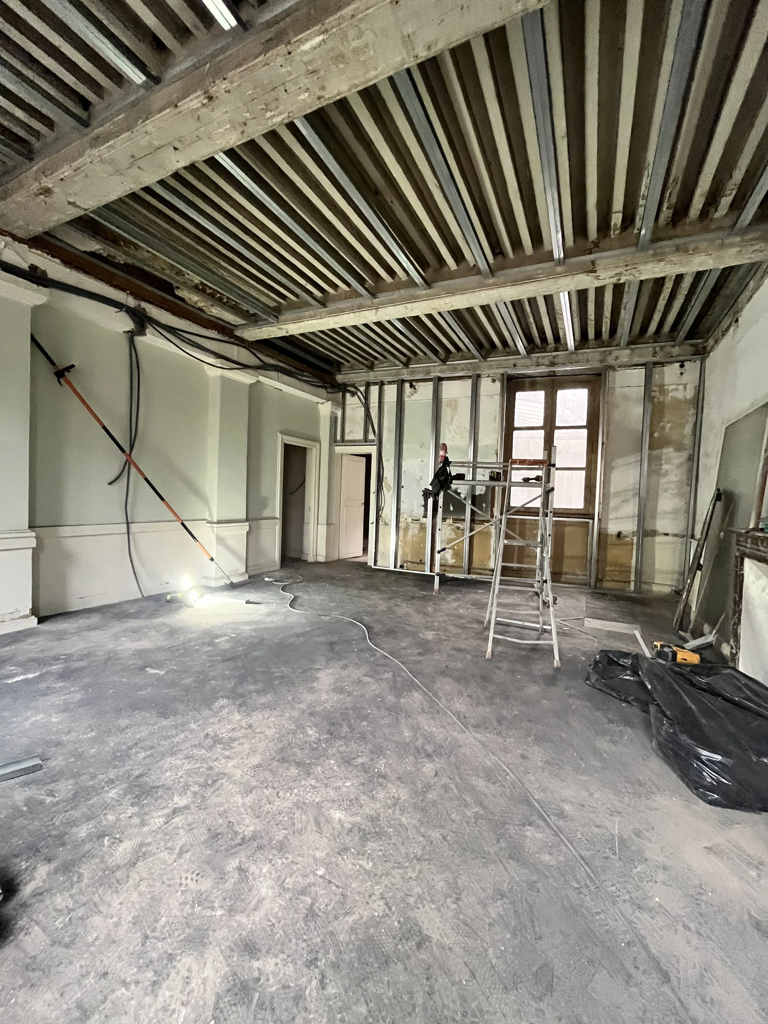 Salle en rénovation avec plafond en cours d'installation, escabeau, outils, et câbles visibles.