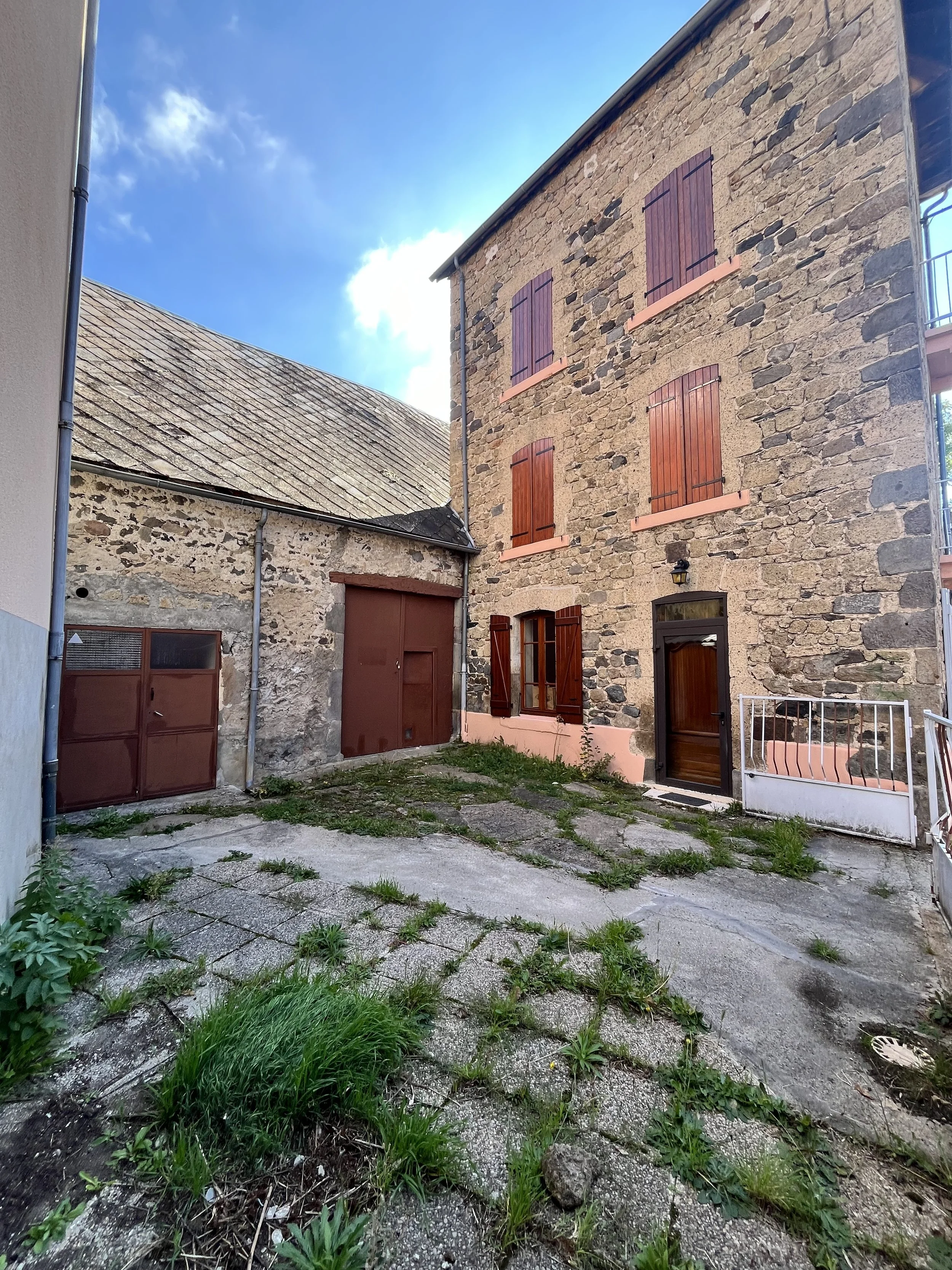 Cour intérieure avec bâtiment en pierre et volets en bois, porte en bois, petits jardins avec herbes et pavés