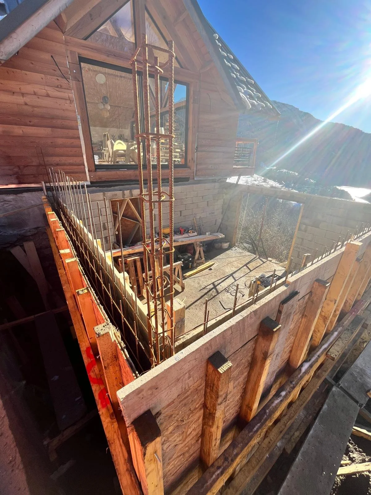 Construction d'une maison en bois avec un balcon en cours de construction sous un ciel ensoleillé.