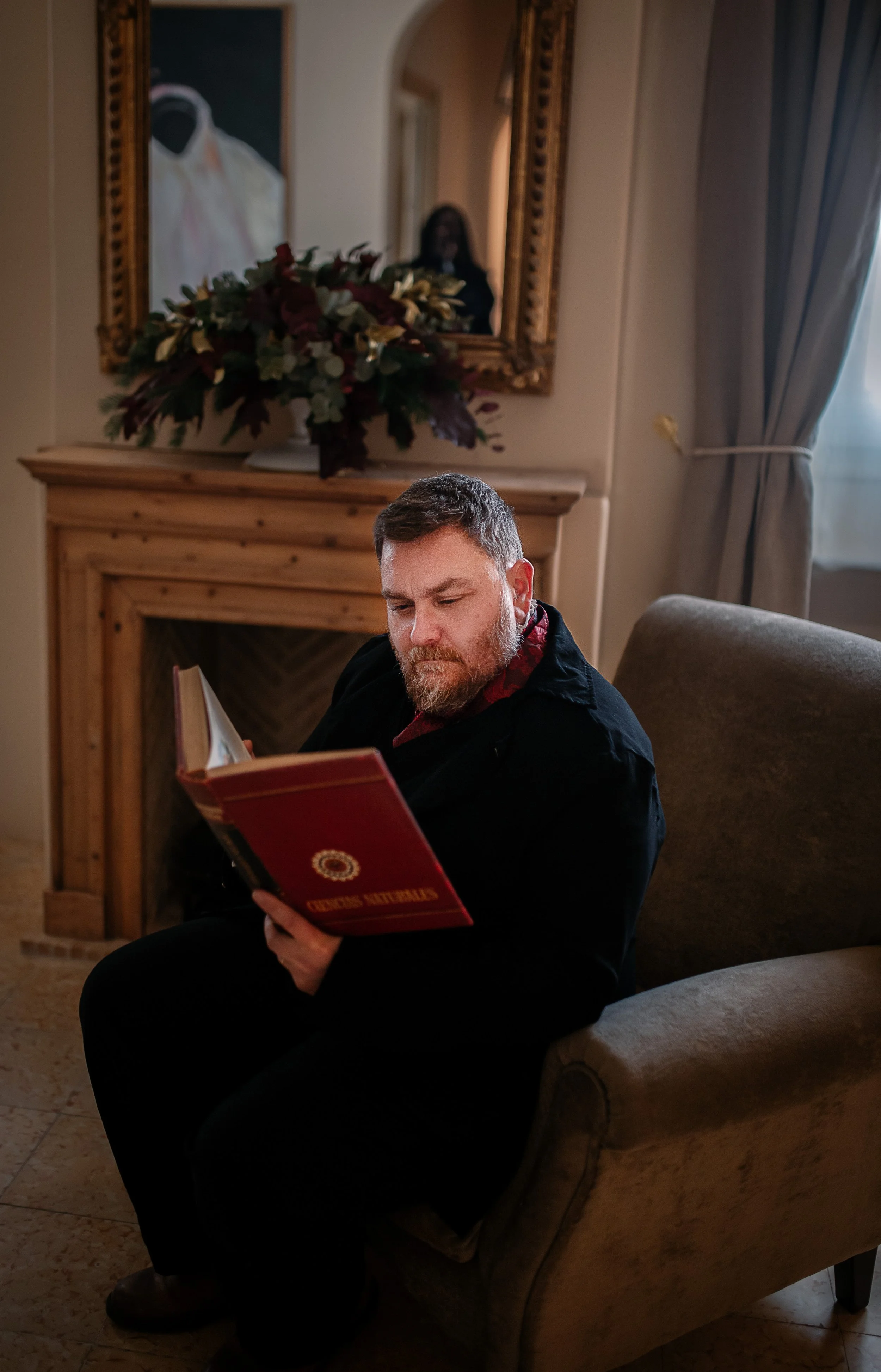 Hombre leyendo un libro en una sala de estar con figura en sombras reflejada en el espejo detrás | ReVolution | Rol en Vivo España