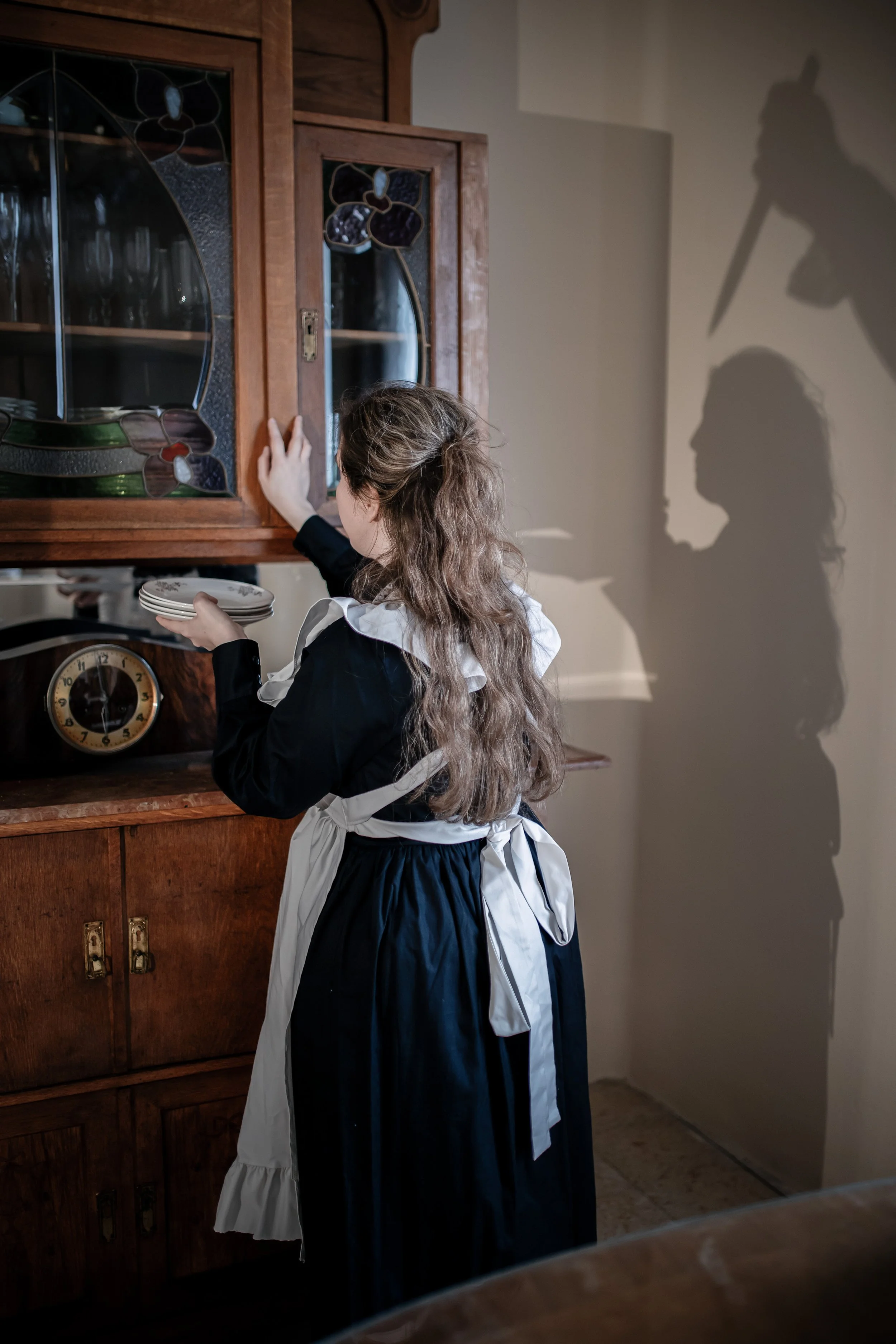 Una niña en un vestido de época colocando platos en un mueble de madera | ReVolution | Rol en Vivo España