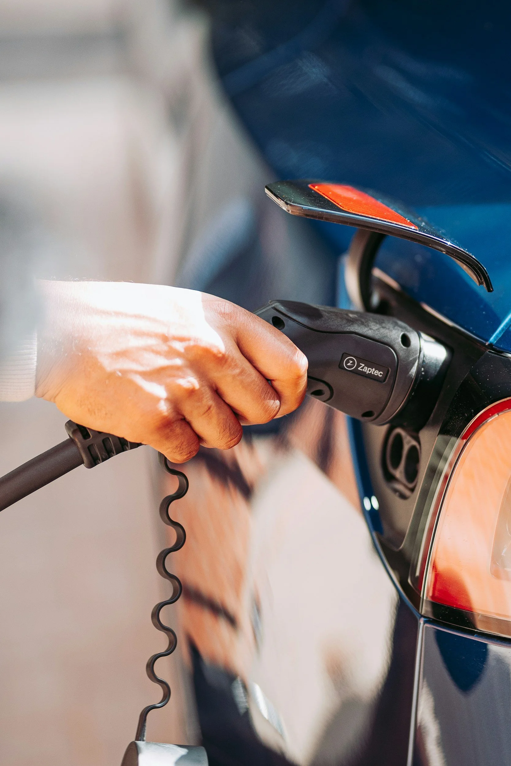 Person charging a blue electric scooter with a Zaptec charging station.