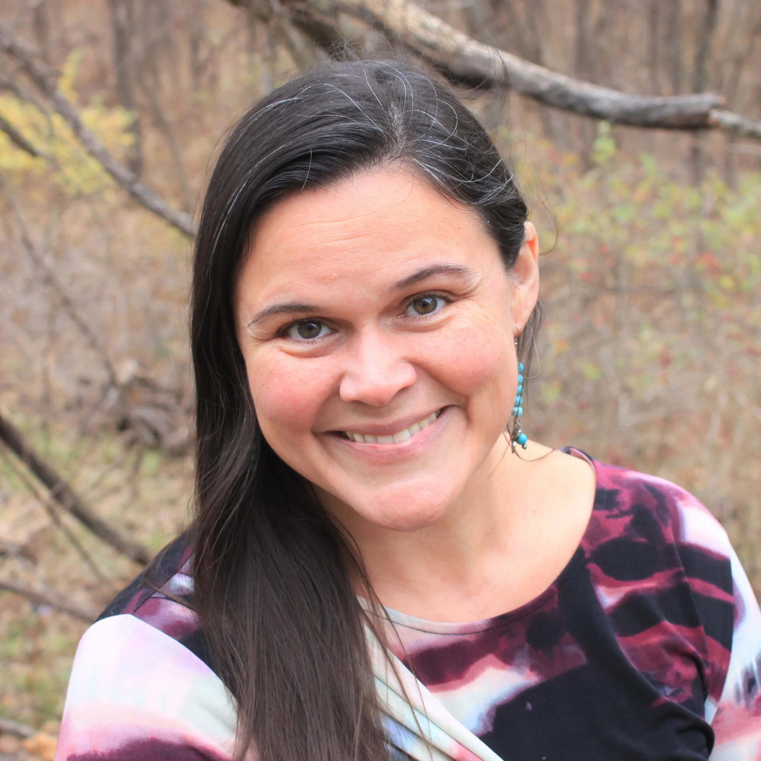 woman with long dark hair, turquoise earrings, and warm smile, forest background