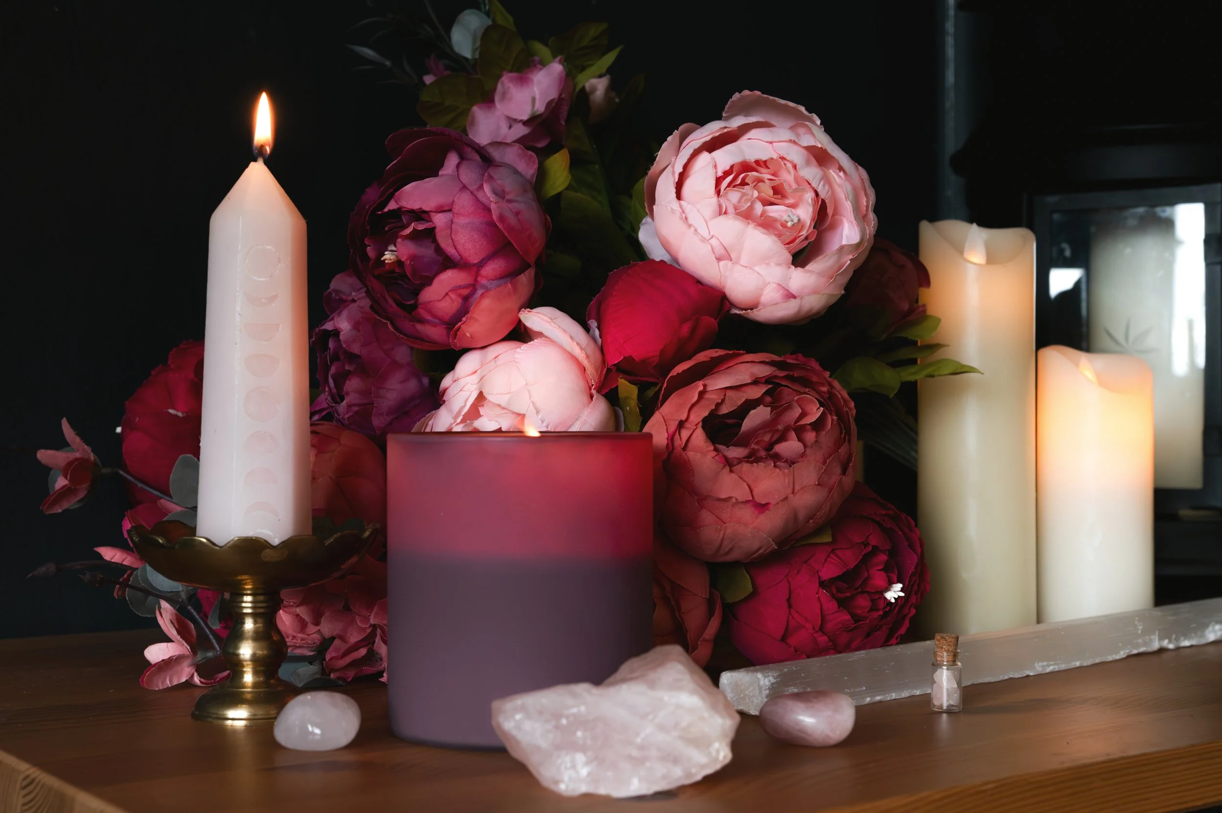Pink candles and rose quartz crystal surrounded by pink peonies.