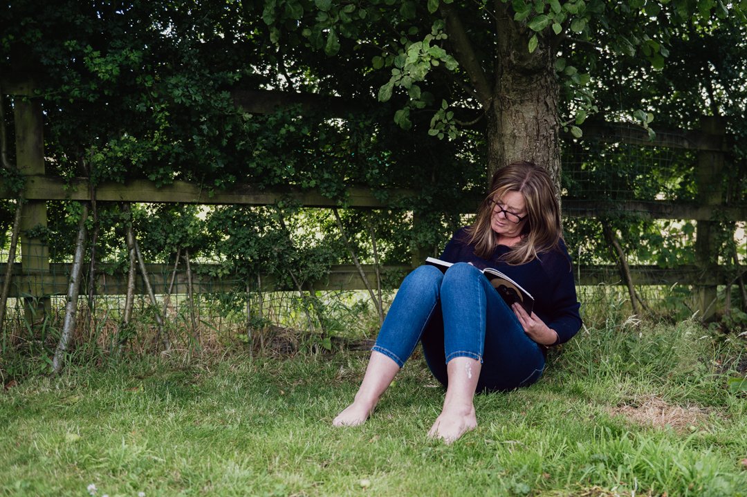 Paula sitting in her garden below an apple tree. She is concentrating, writing in her journal