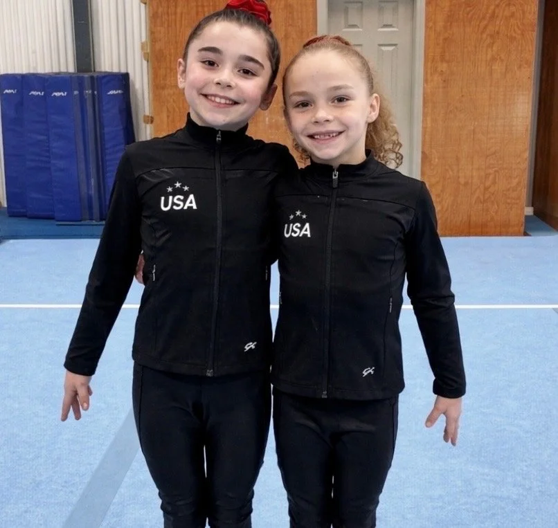 Two girls standing side by side in black USA gymnastics gym clothes