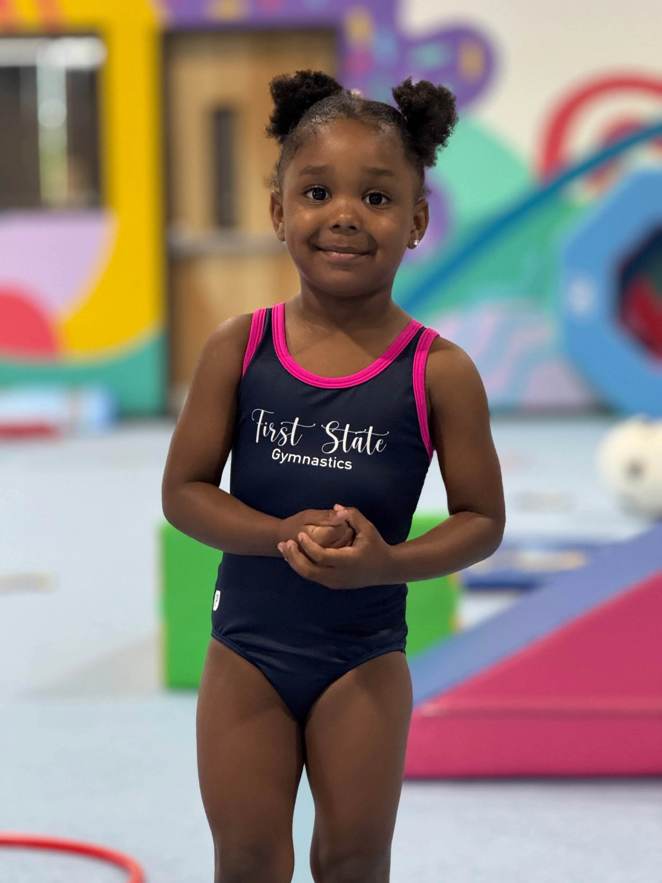 Little girl in black First State Gymnastics leotard smiling.
