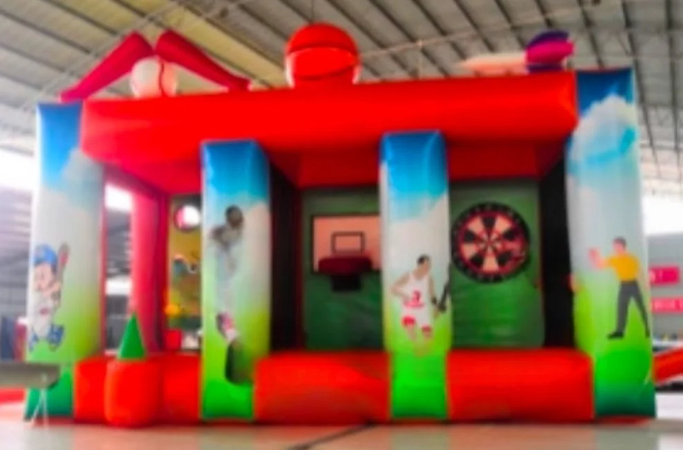 Inflatable bounce house with sports theme, featuring a basketball hoop and dartboard, decorated with cartoon characters and vibrant colors.