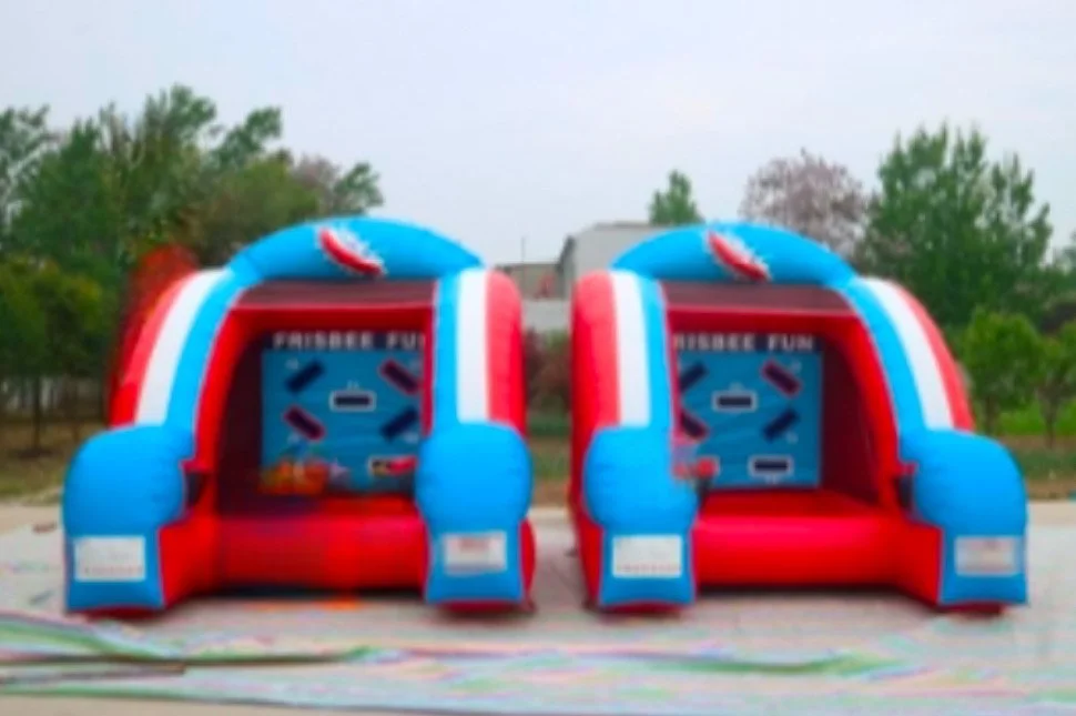 Two inflatable bounce houses decorated with red, white, and blue colors, set up outdoors with trees and a cloudy sky in the background.