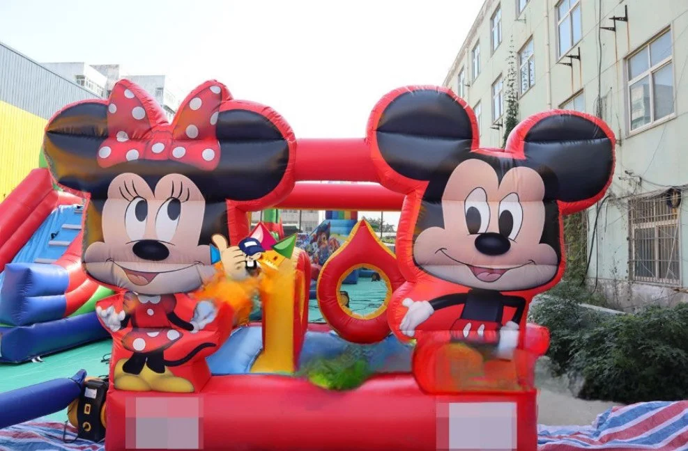 Inflatable bounce house with Minnie Mouse and Mickey Mouse designs, set outdoors in an urban area with surrounding buildings.