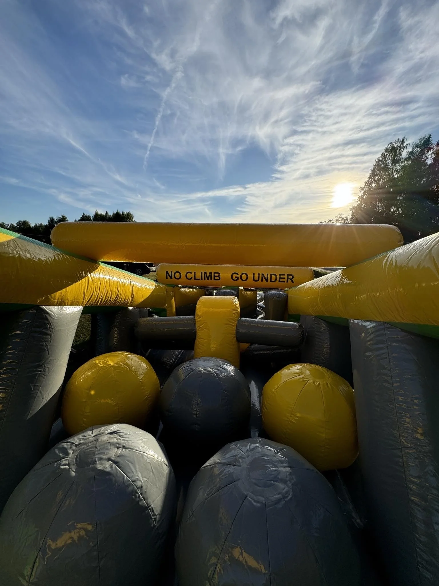 Inflatable obstacle course outdoors with a sign that reads 'NO CLIMB GO UNDER' during sunset.