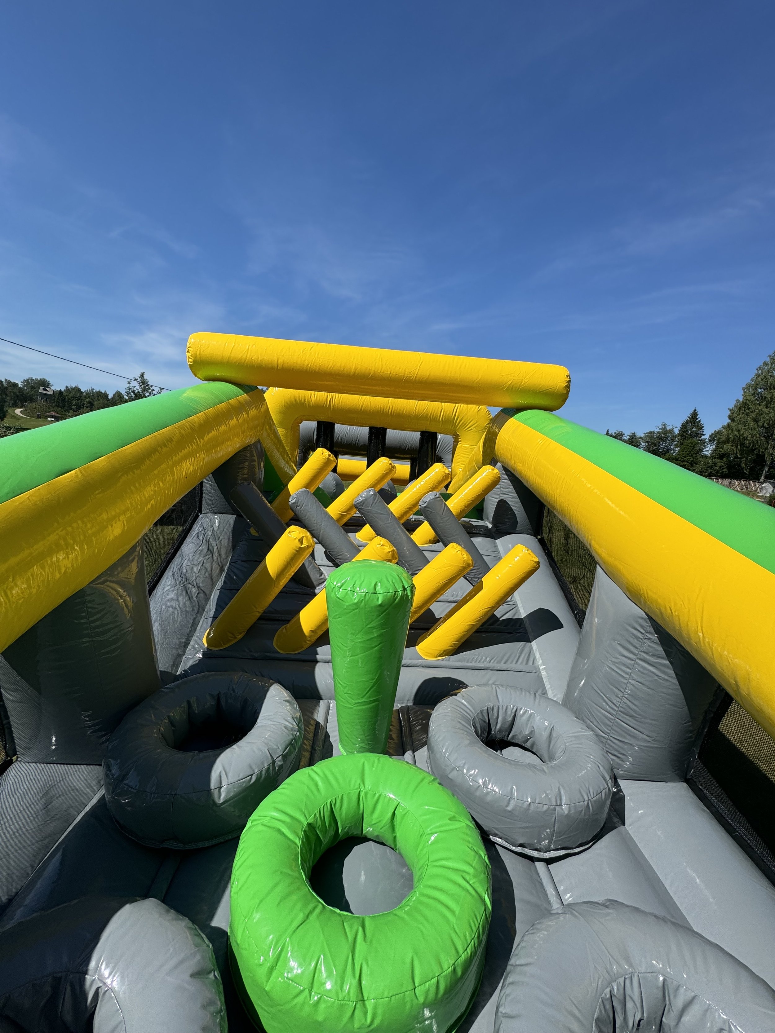 A colorful inflatable obstacle course outdoors under a blue sky with trees in the background.