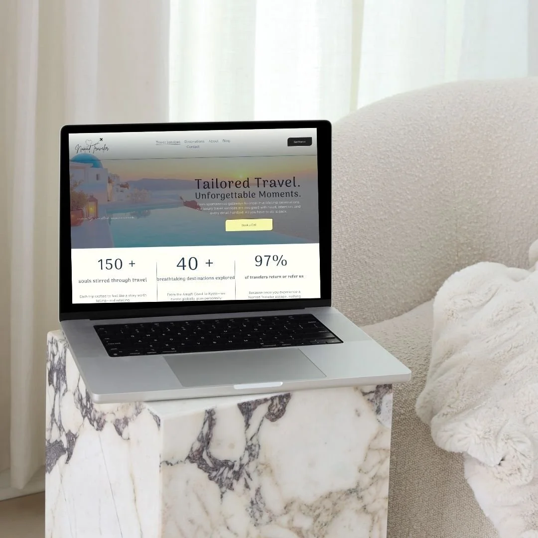 A laptop on a marble side table displaying a travel website, next to a light-colored sofa with a white blanket.