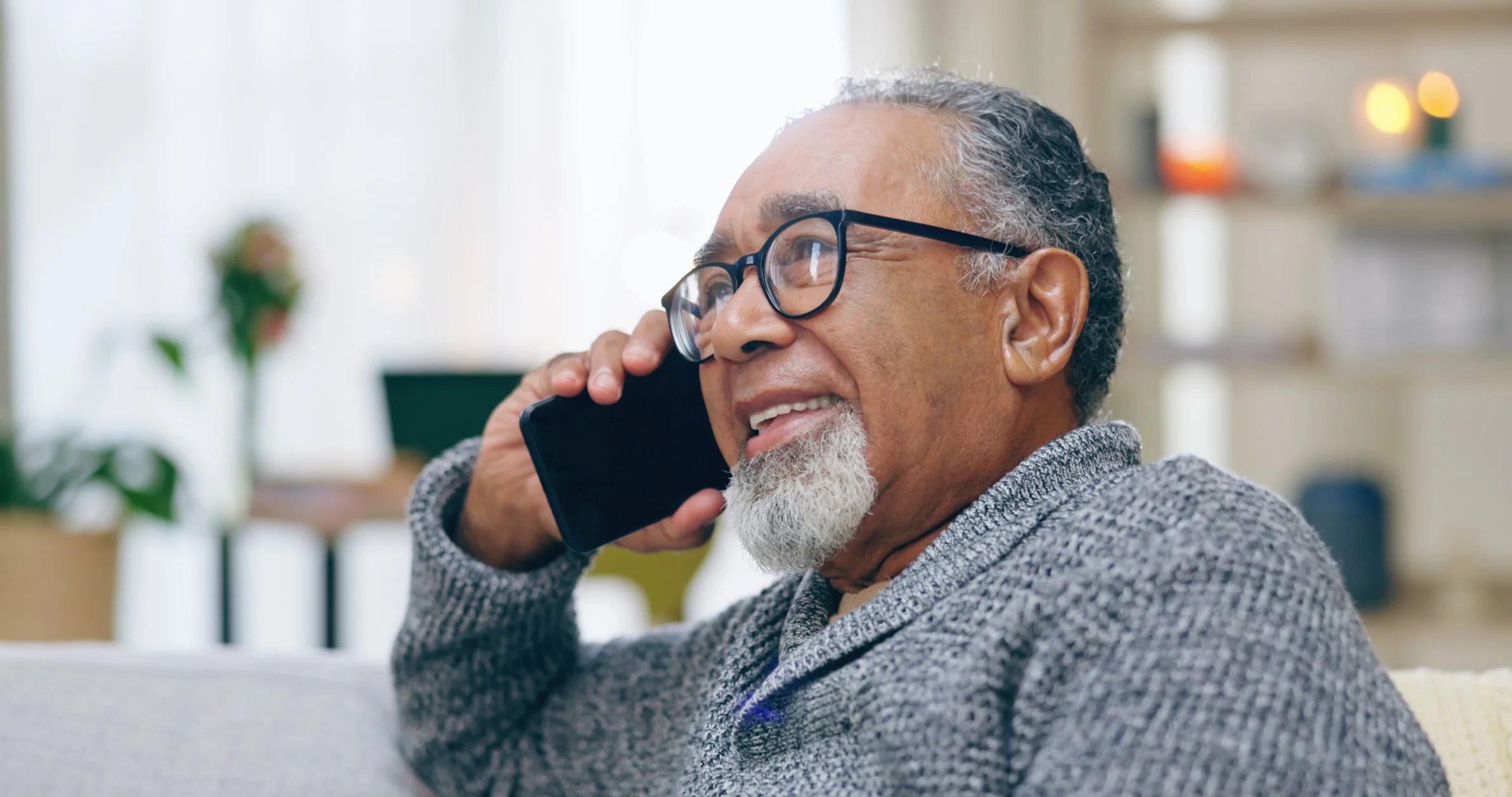 Smiling older man with glasses talking on a phone indoors.