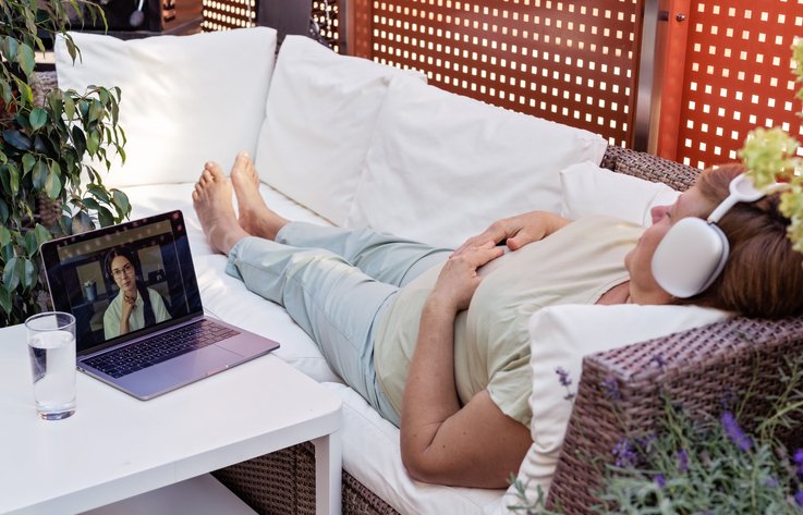 Person relaxing on a sofa with headphones, watching laptop