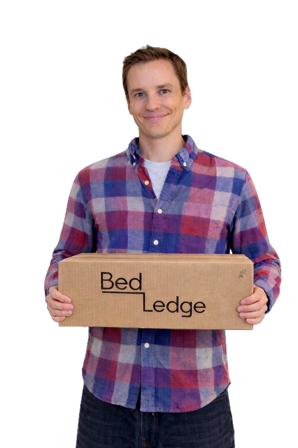 A young man wearing a plaid shirt holds a cardboard box with the words "Bed Edge" printed on it, smiling at the camera.