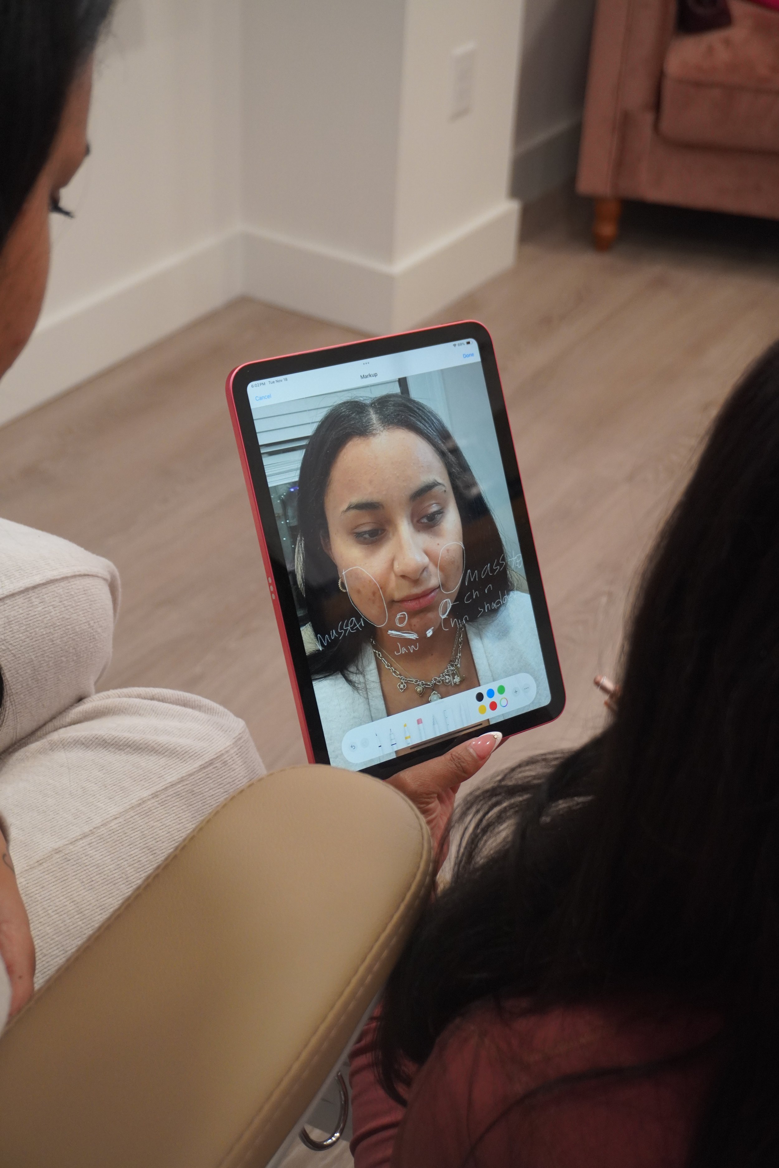 A nurse injector shows a patient a facial analysis on a tablet during an aesthetic treatment consultation.