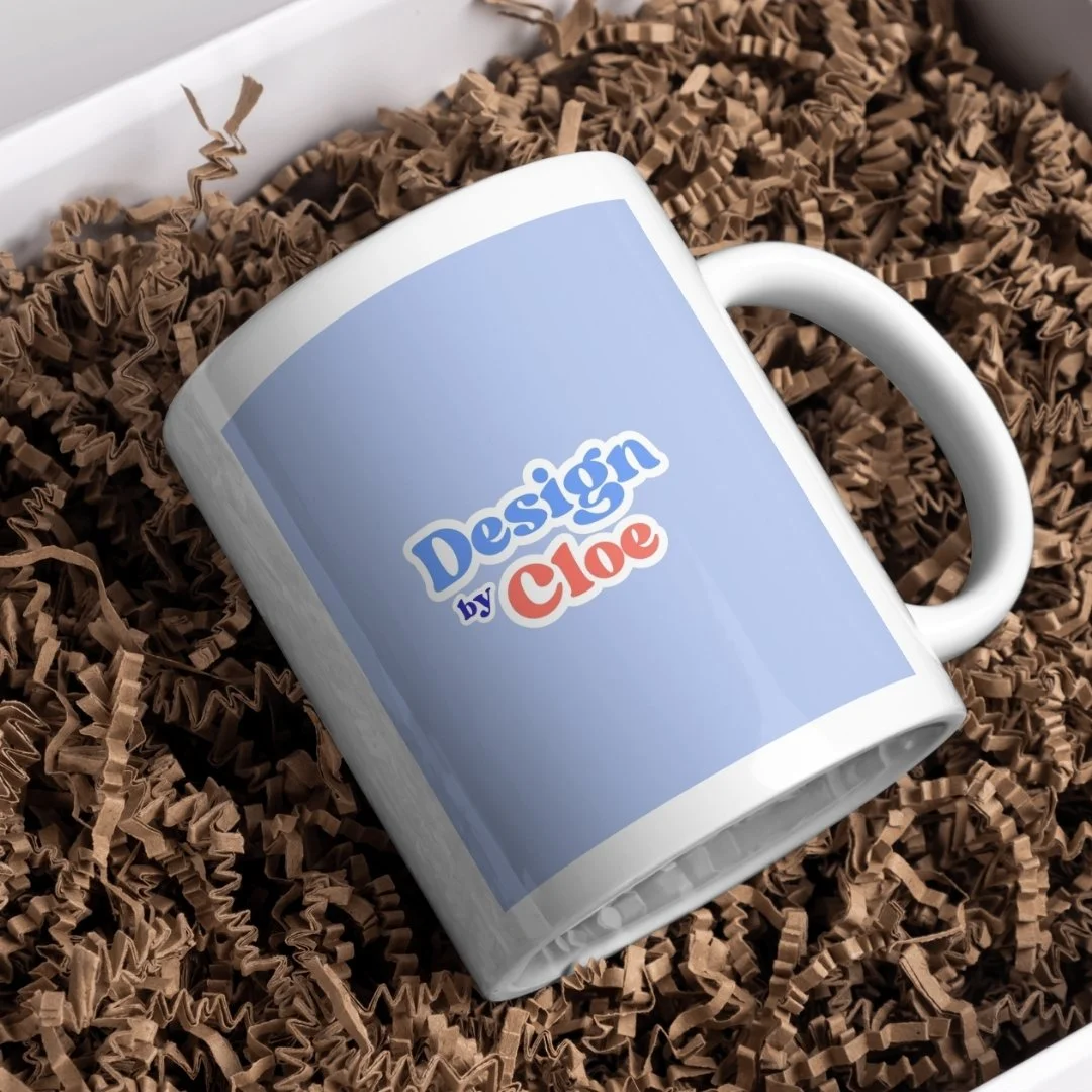 Une tasse blanche avec un design personnalisé intitulé 'Design by Cloe', placée sur de la papier de soie brune dans une boîte d'emballage.