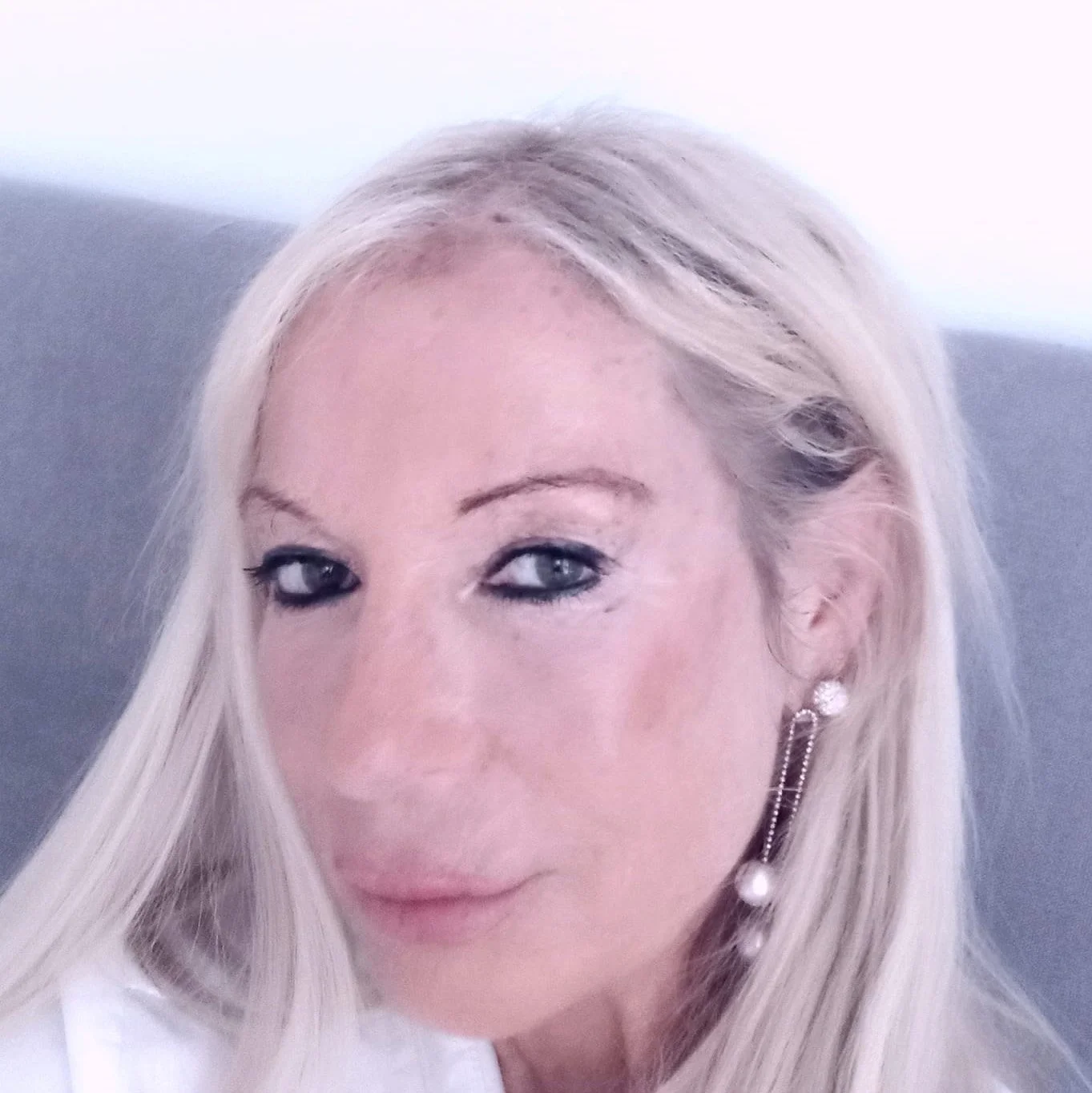 Close-up of a woman with long blonde hair, light skin, and wearing pearl earrings and makeup.