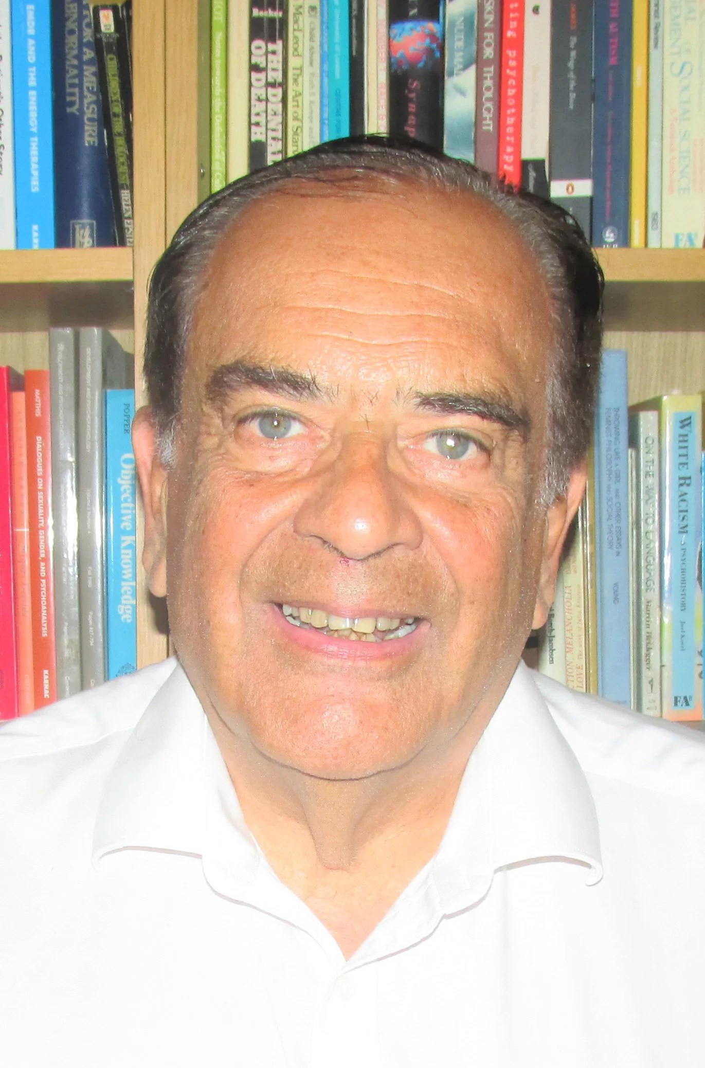 Portrait of a man with gray hair and blue eyes in front of a bookshelf filled with colorful books.