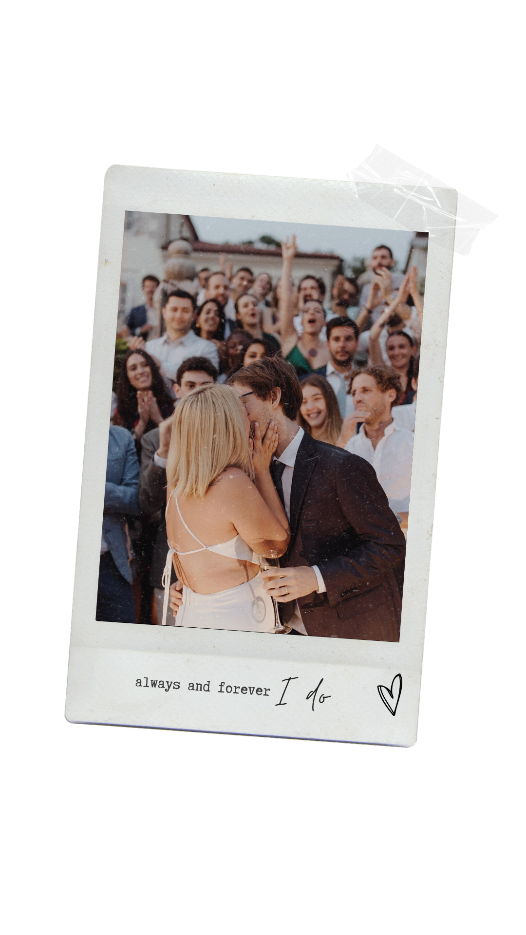A Polaroid photo showing a wedding celebration with a bride and groom kissing, surrounded by a large group of cheering guests in an outdoor setting. The caption reads, "always and forever I do" with a heart doodle.