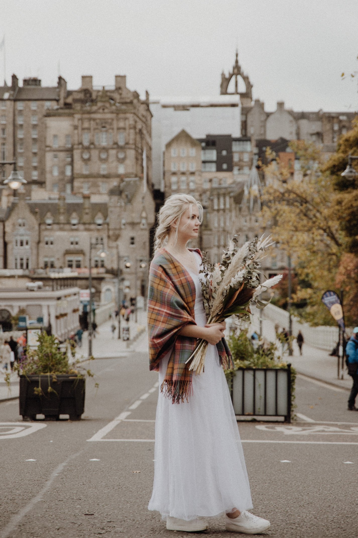  bridal photo portrait of blonde model walking in edinburgh old town Royal Mile with a bouquet of dried flowers in arm and edinburgh old town in the background 