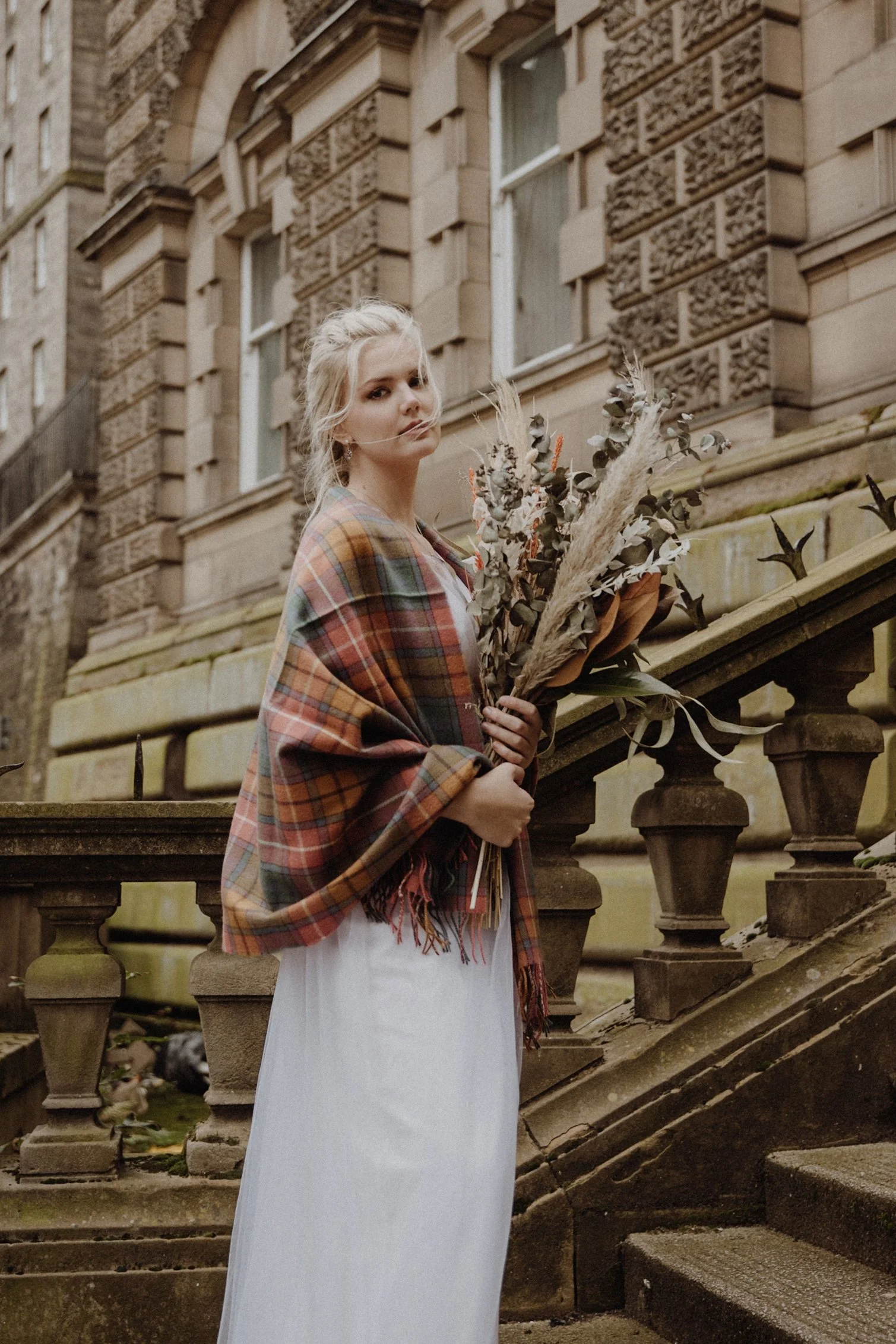  bridal photo portrait of blonde model walking in edinburgh old town Royal Mile with a bouquet of dried flowers in arm and edinburgh old town in the background 
