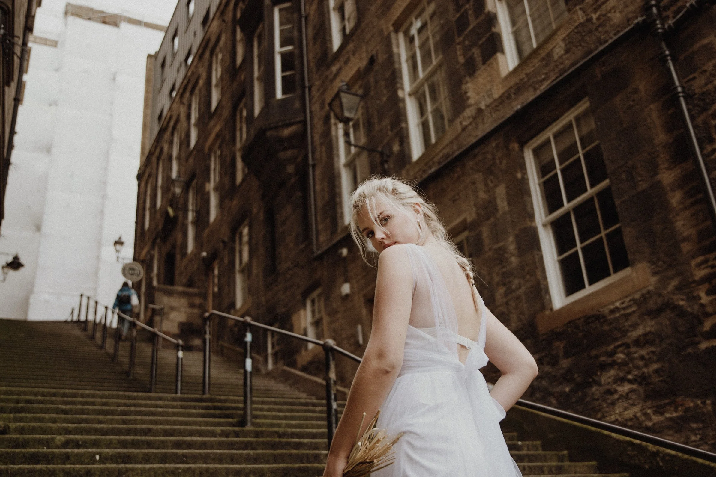 bridal photo portrait of blonde model walking in edinburgh old town Royal Mile with a bouquet of dried flowers in arm and edinburgh old town in the background 