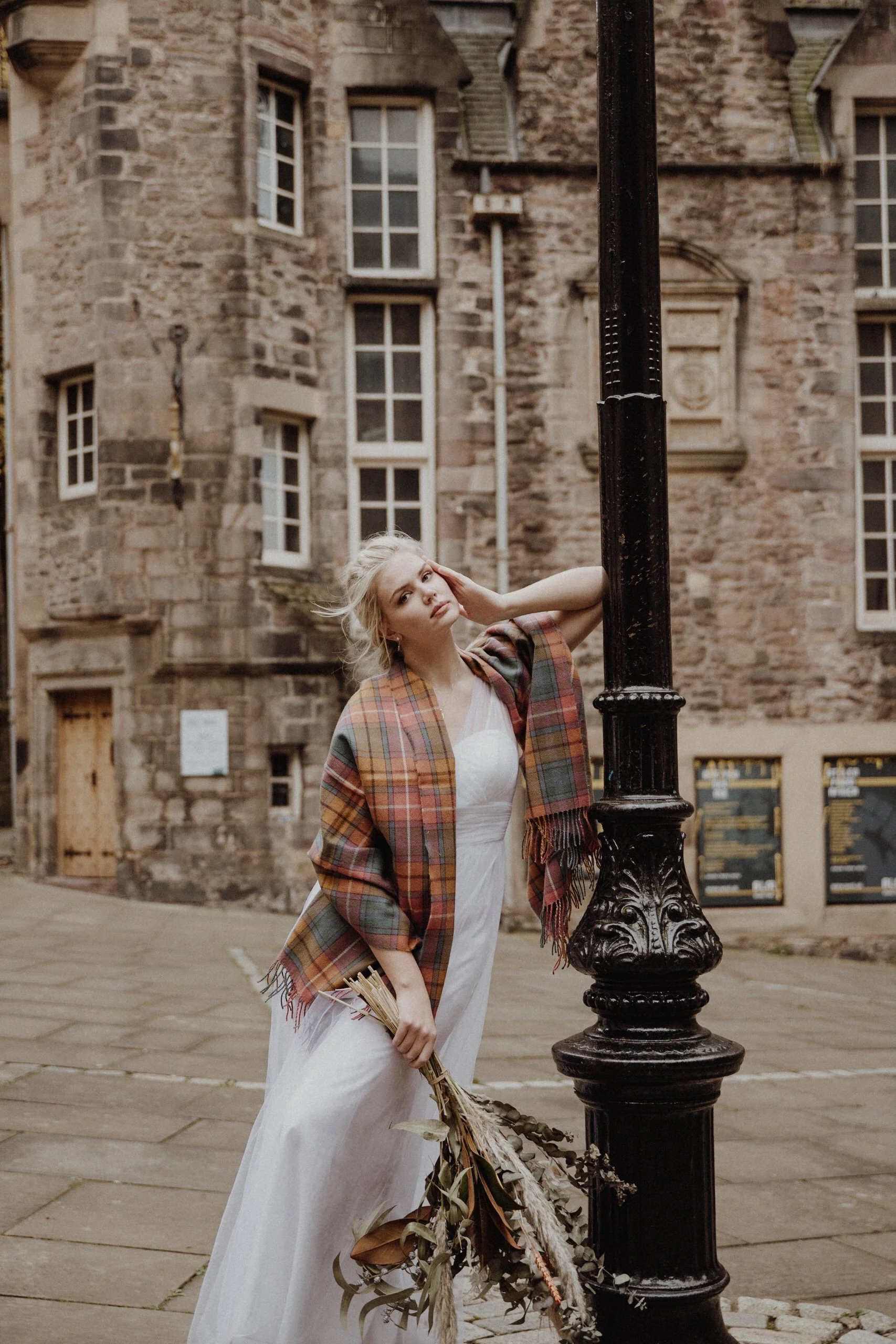  bridal photo portrait of blonde model walking in edinburgh old town Royal Mile with a light camel coat and a bouquet of dried flowers in arm 
