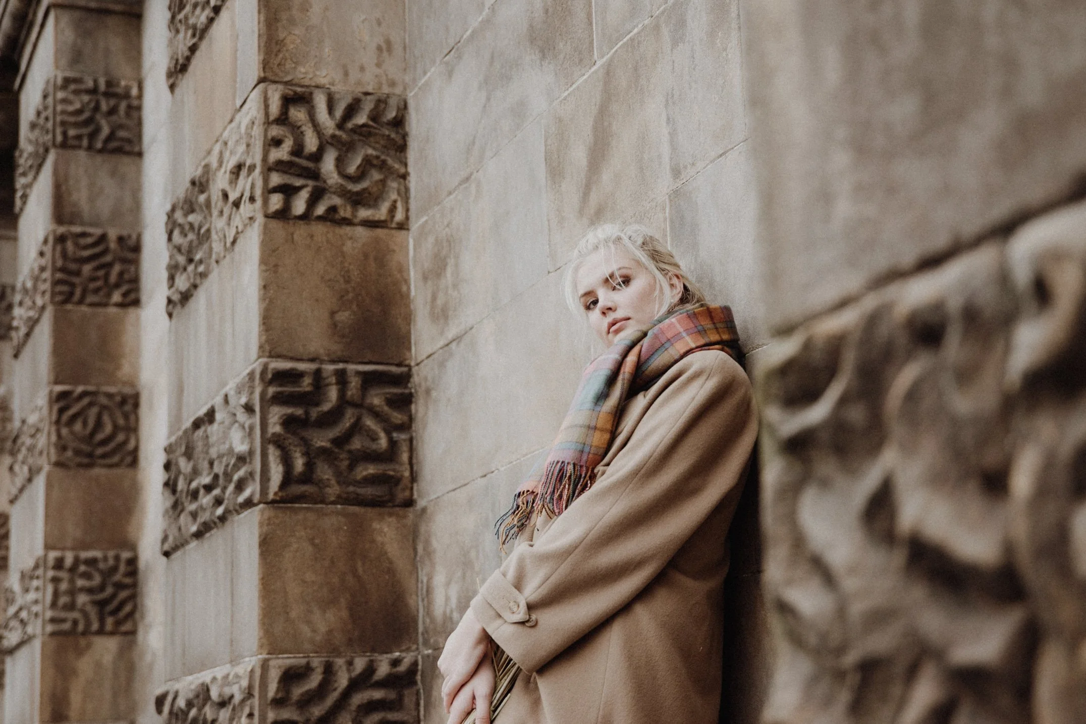  bridal photo portrait of blonde model walking in edinburgh old town Royal Mile with a light camel coat and a bouquet of dried flowers in arm 