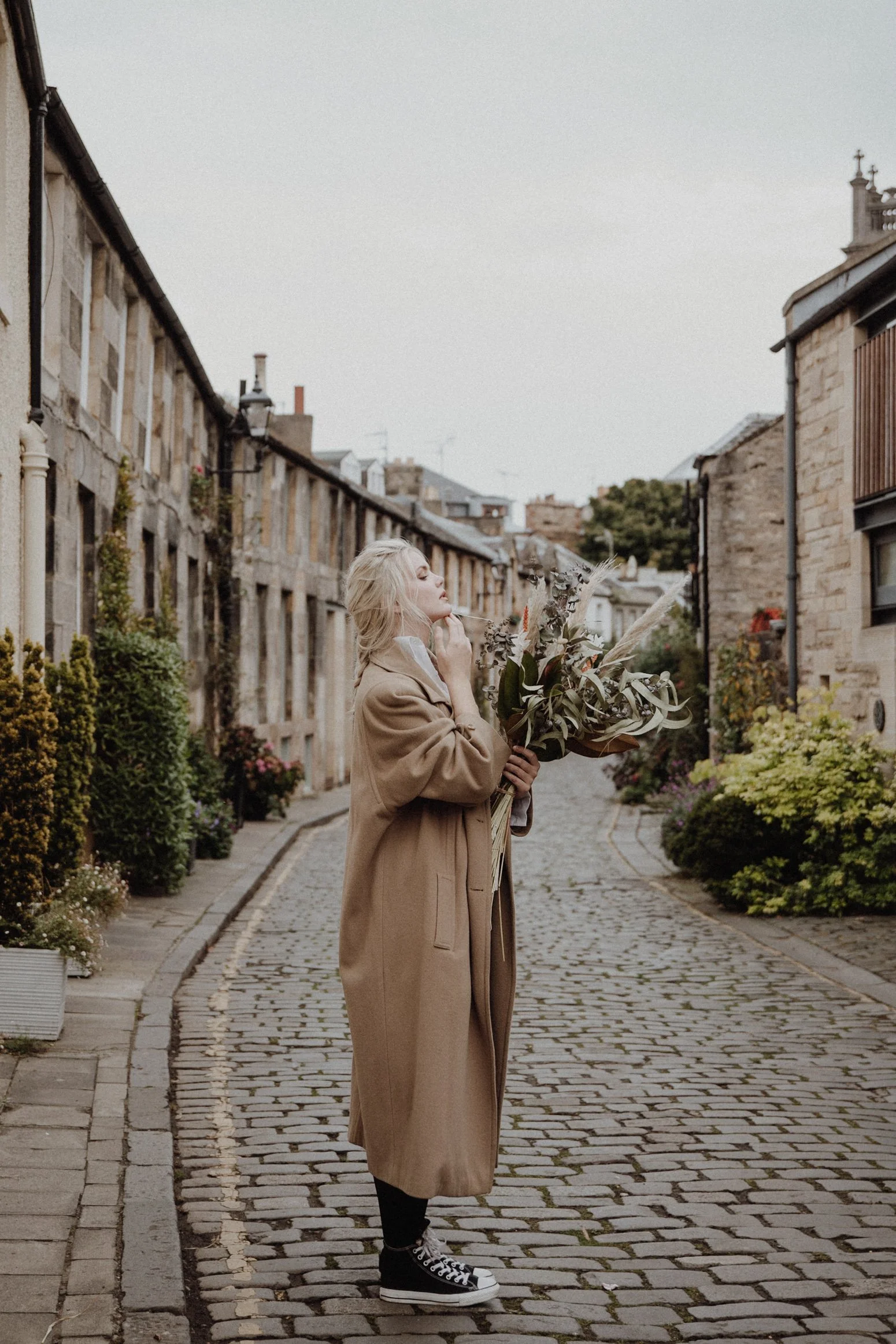  photo portrait of blonde model walking in edinburgh new town Circus Lane with a light camel coat and a bouquet of dried flowers in arm 