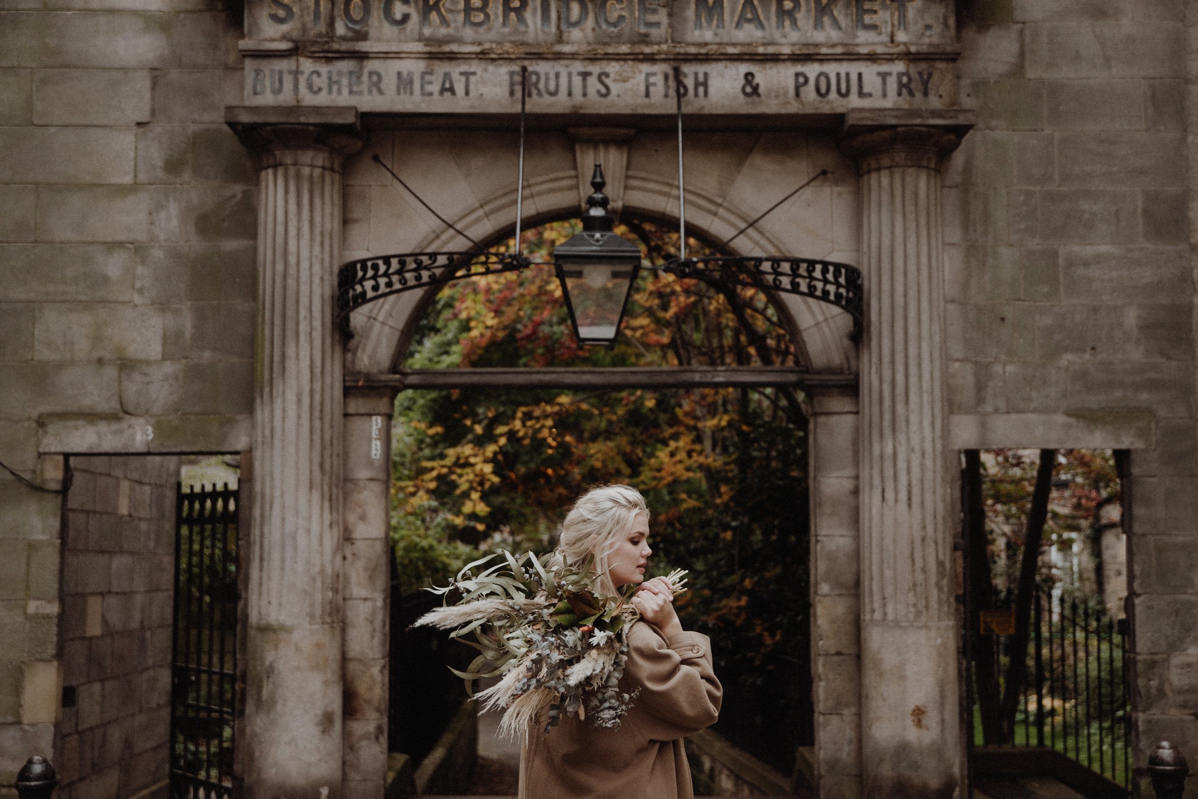  photo portrait of blonde model walking in edinburgh new town Stockbridge with a light camel coat and a bouquet of dried flowers in arm 