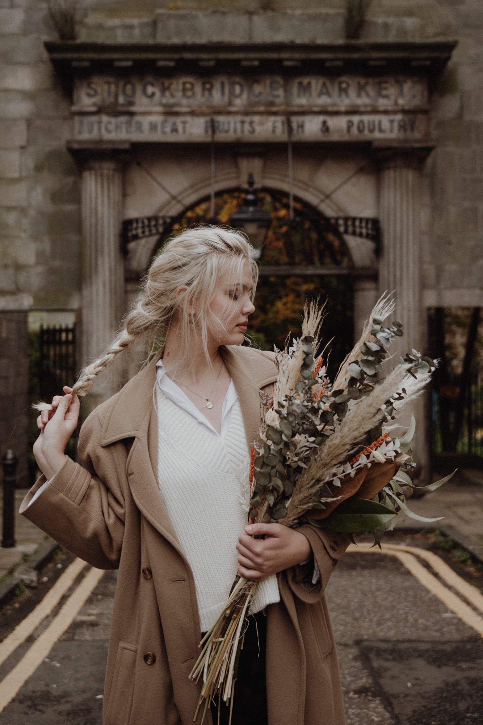  photo portrait of blonde model walking in edinburgh new town Stockbridge with a light camel coat and a bouquet of dried flowers in arm 
