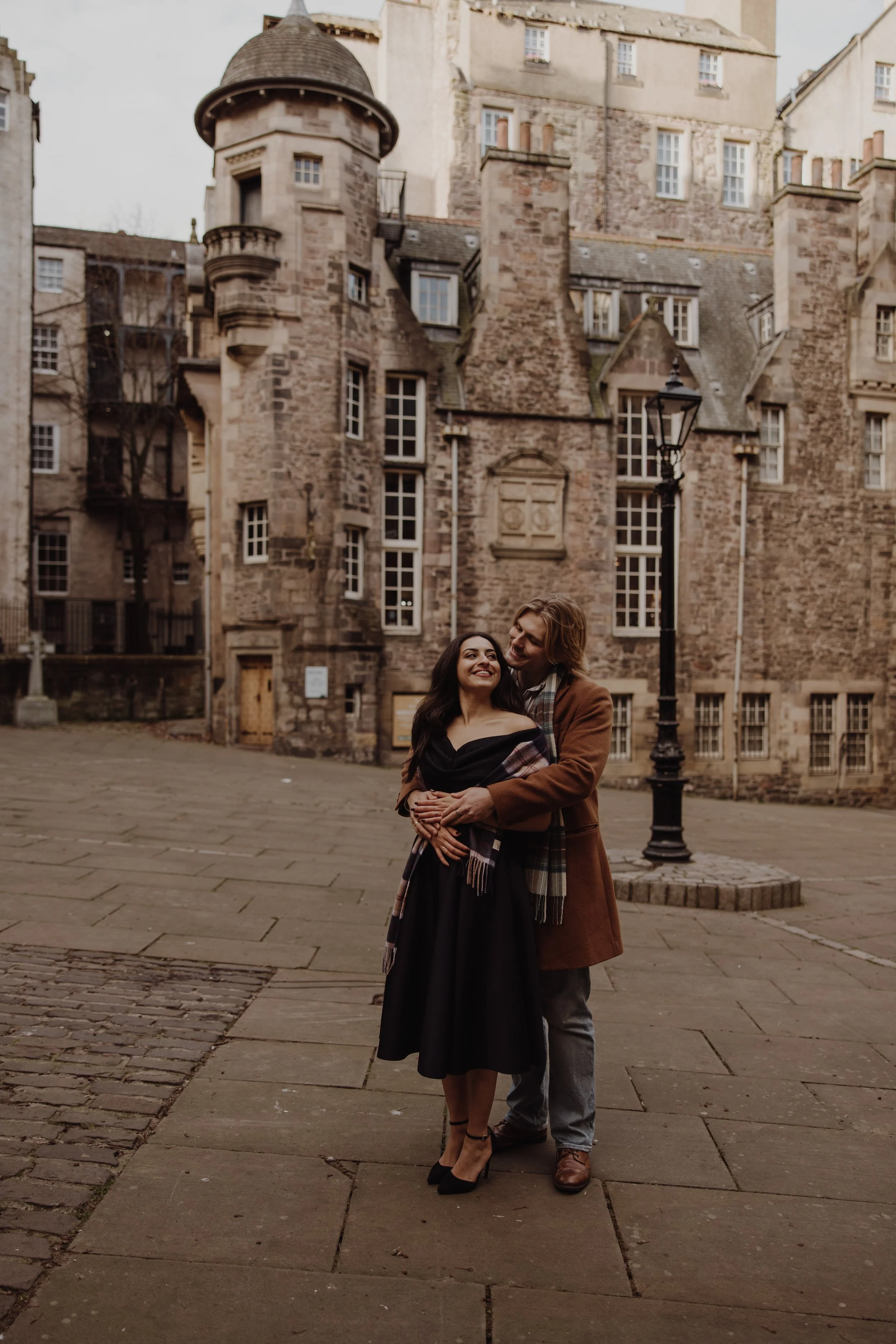 stylish couple with smart outfits hugging against iconic Edinburgh writer's museum backdrop