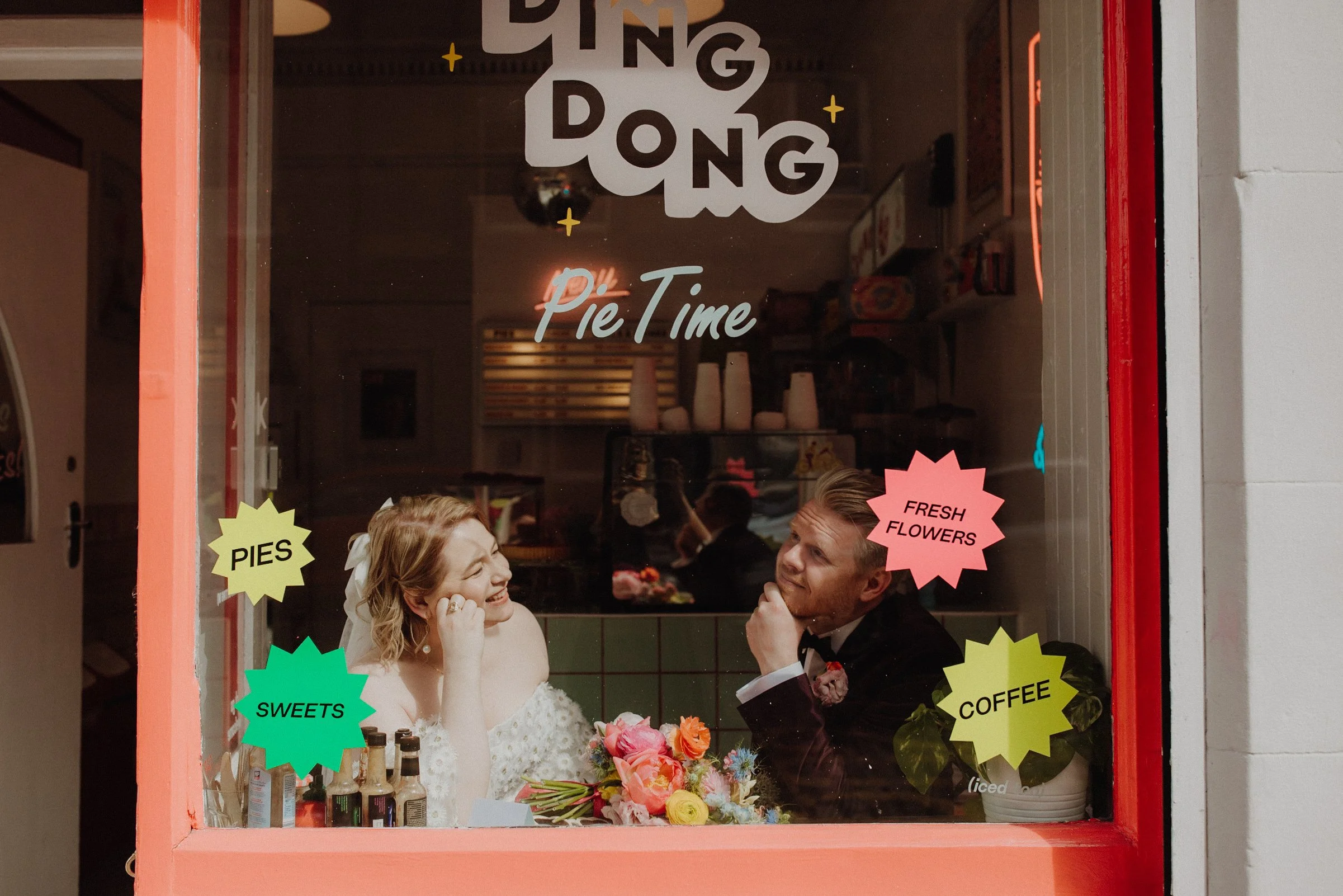 bride and groom couple sitting in a 50's style diner window looking outside smiling on their wedding day, in iconic Leith pie shop