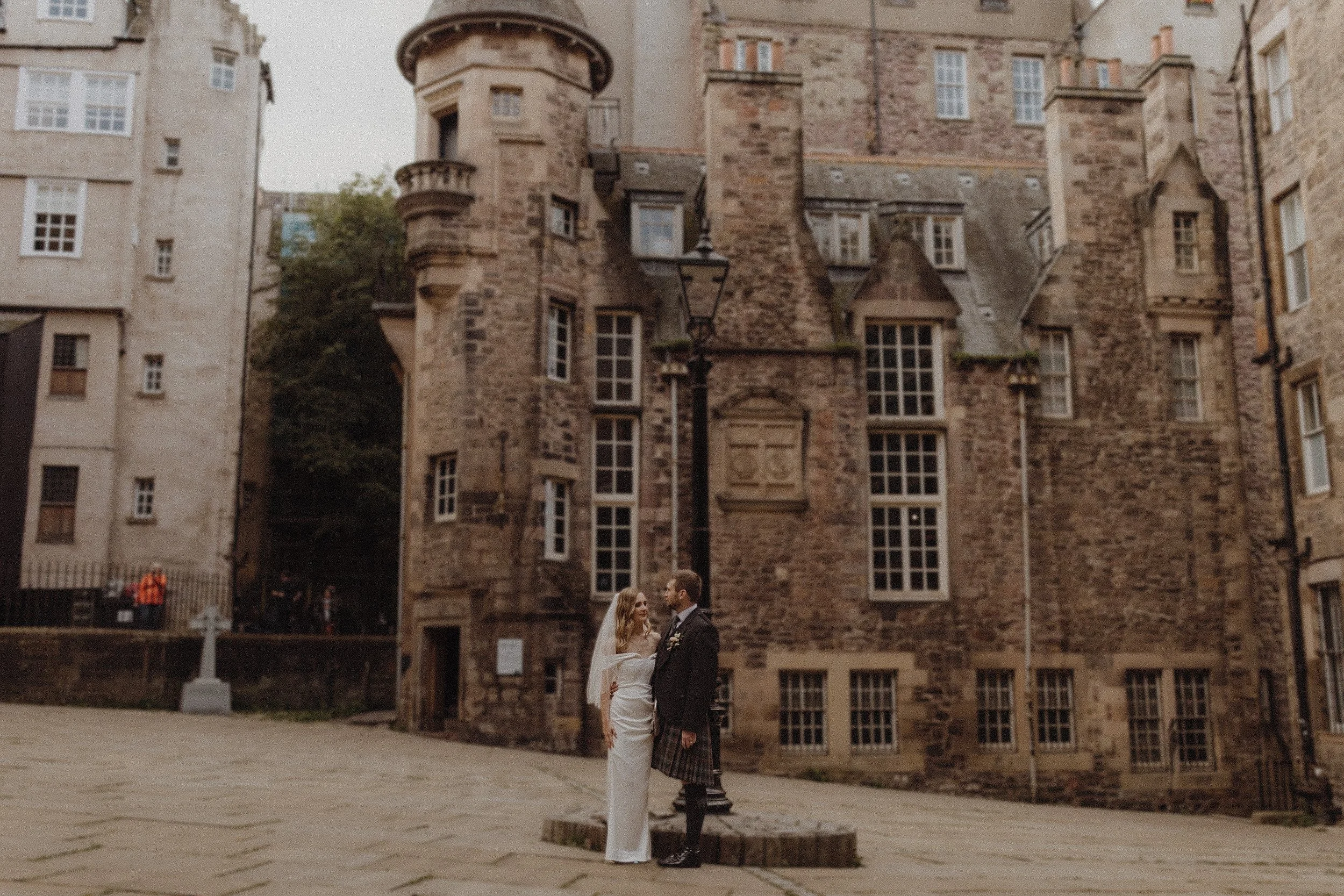 Stunning bride in corset dress and groom in kilt standing in iconic edinburgh spot in front of the writers museum during their wedding portraits