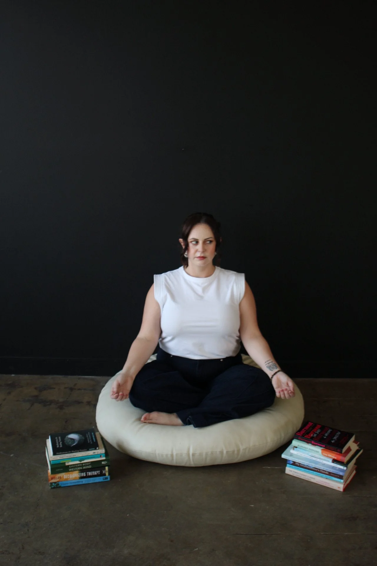 Therapist sitting cross legged in meditation between stacks of mental health books representing burnout recovery and emotional balance for therapists and caregivers in Texas