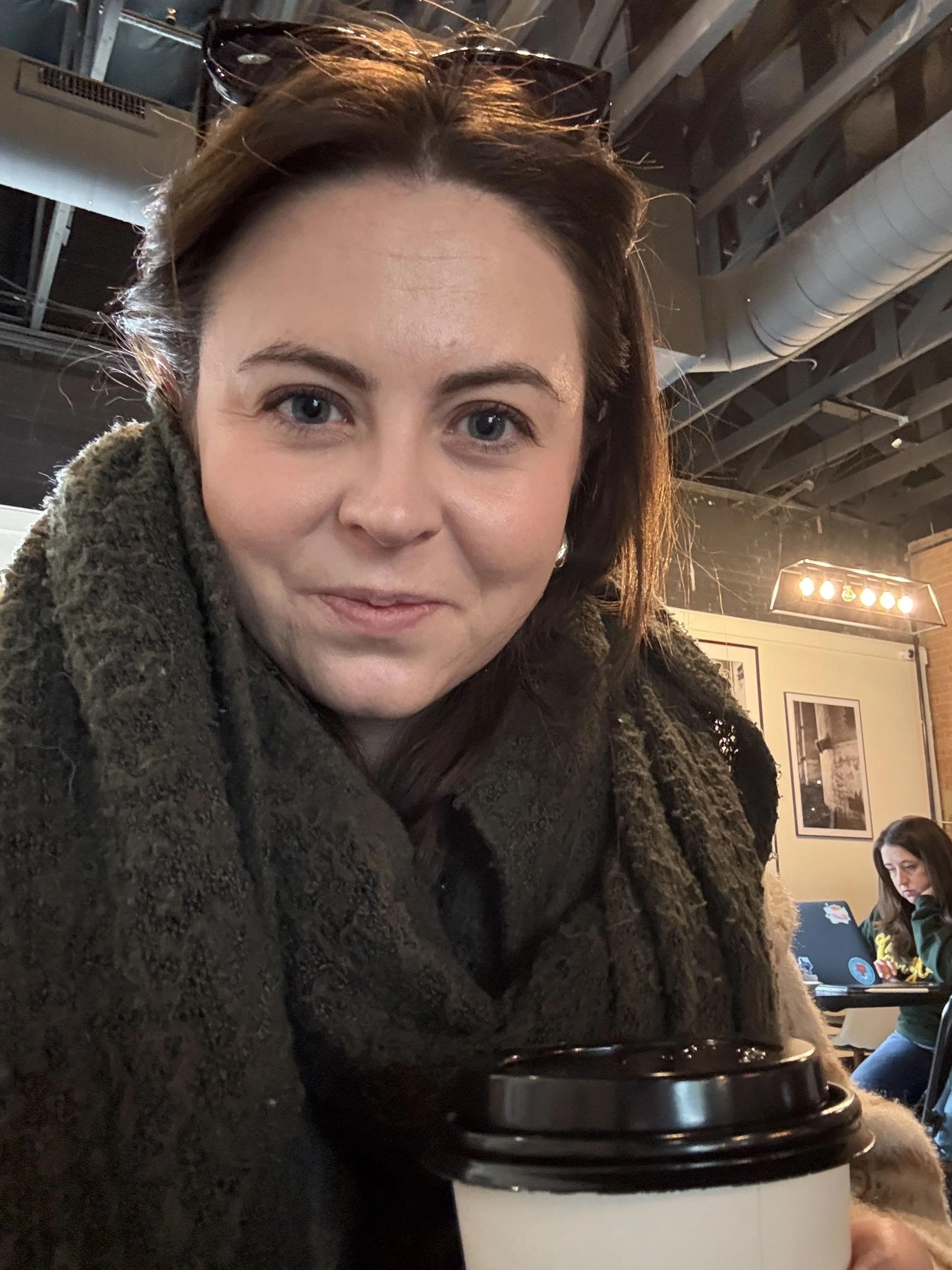 Woman holding coffee in a cozy café reflecting on relationship patterns and emotional availability in therapy for helpers