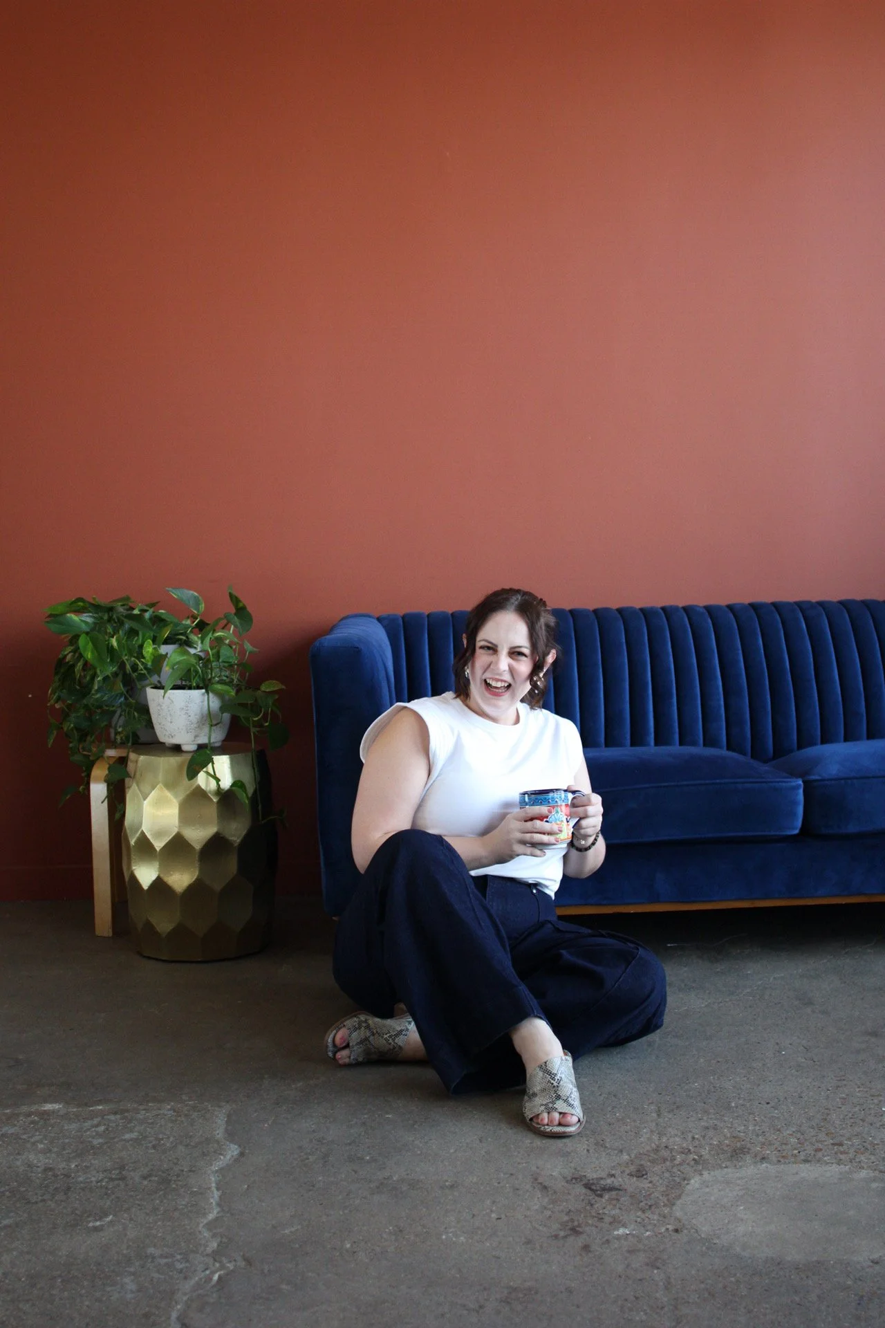 Aubrey Richardson, therapist in Texas, sitting on the floor by a blue couch holding a mug, representing burnout therapy for high-achieving professionals