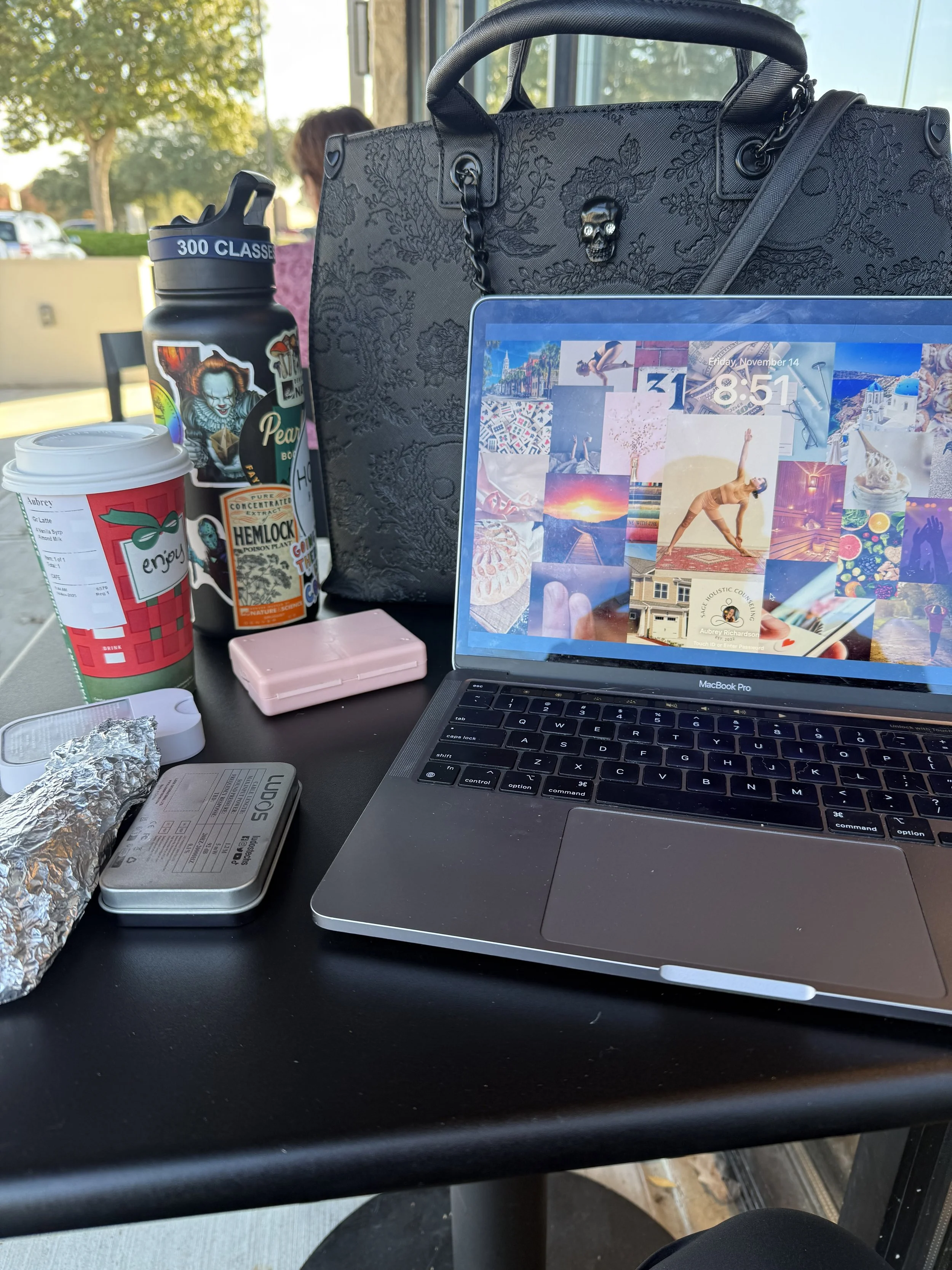 Laptop and work setup at a café with coffee and water bottle representing burnout, overworking, and constant productivity in high-achieving professionals