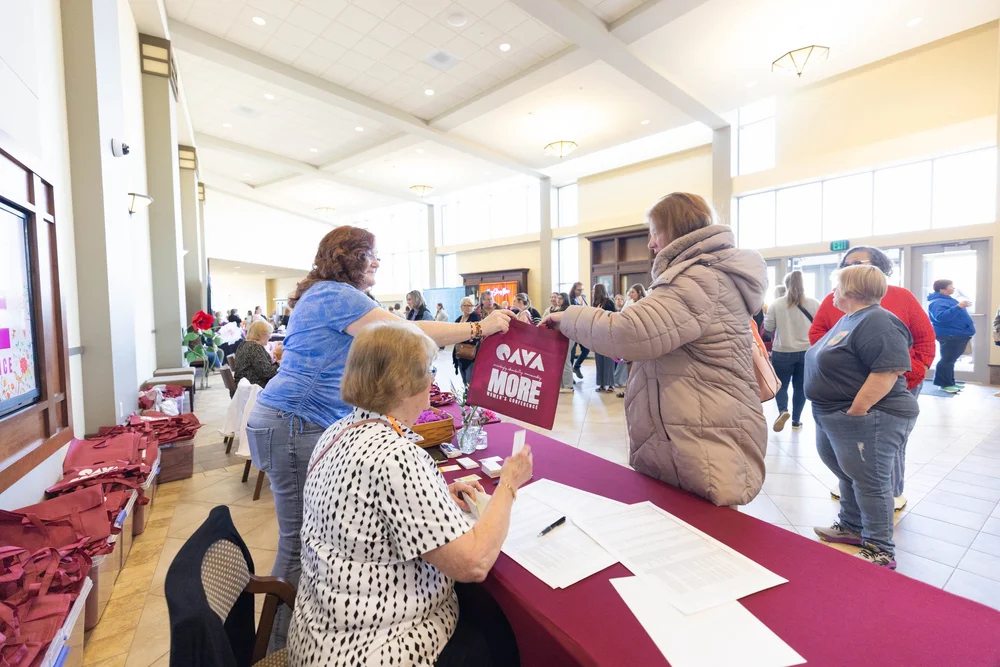 Volunteers at the registration table hand a MORE tote bag across to an arriving guest.