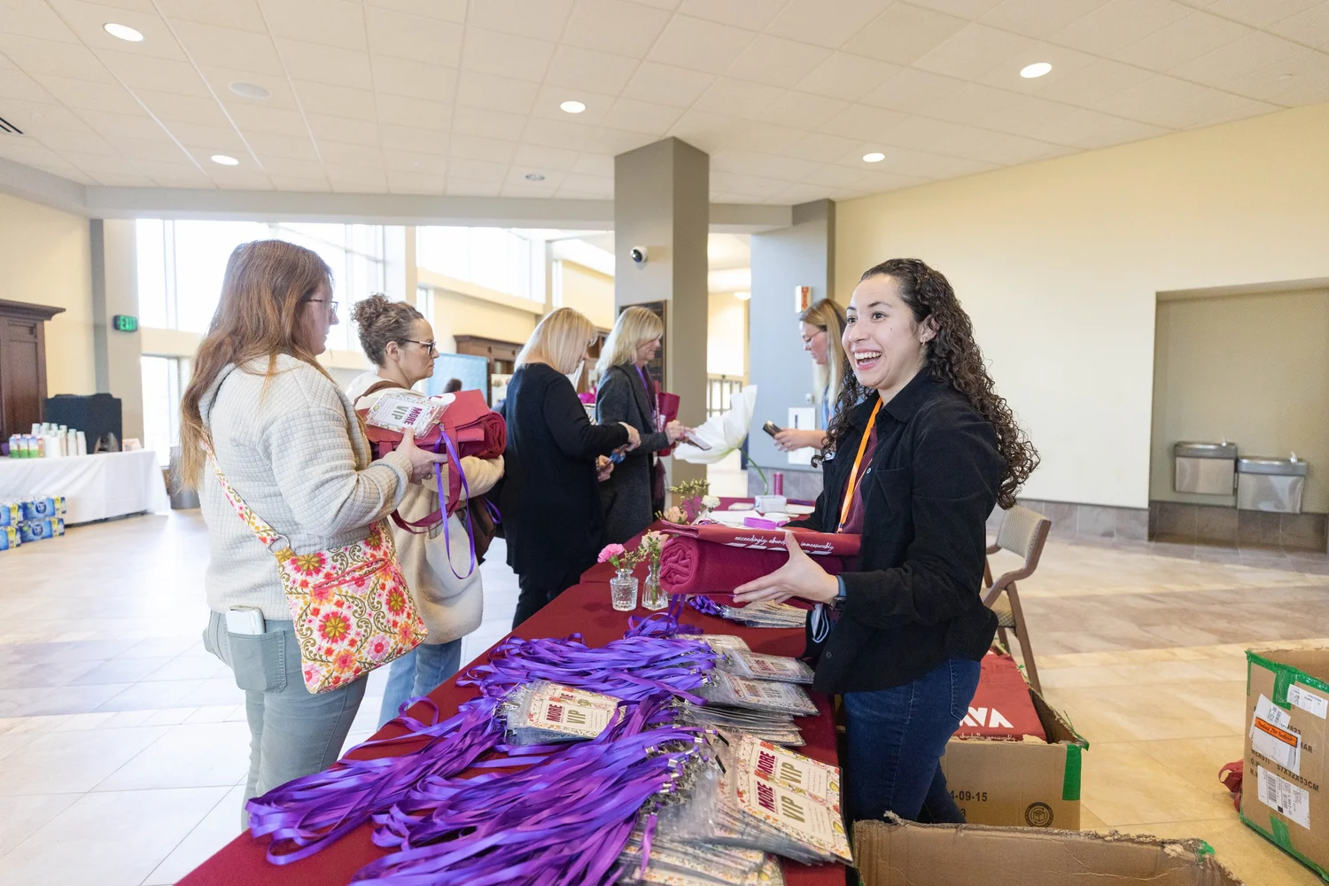 A smiling MORE volunteer hands out lanyards and welcome bags to women arriving at the check-in table.