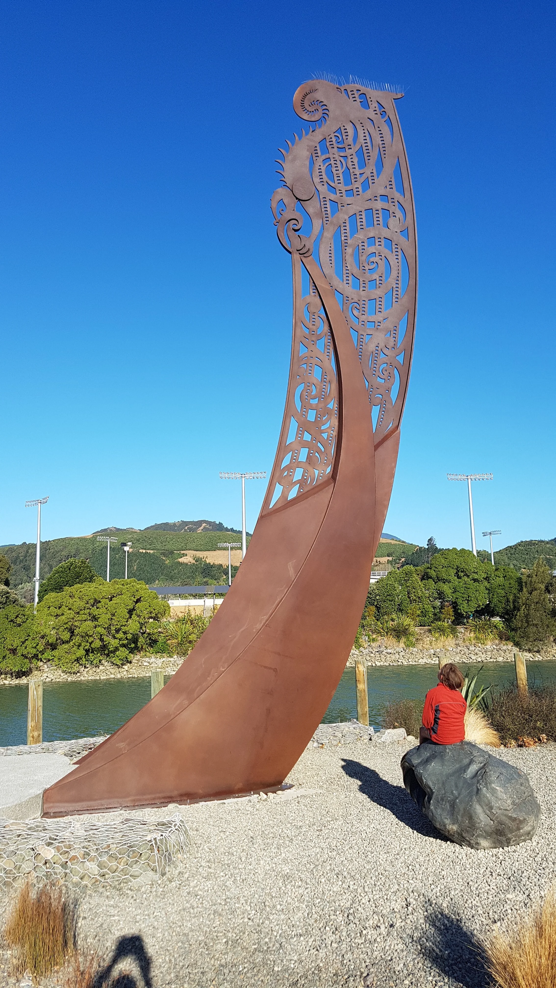 Cortin steel sculpture of Taupara (Waka prow) designed by artist Maia Heggland and refined detailing for steel-cutting by architectural designer Keni-Duke Hetet, maitai river in background