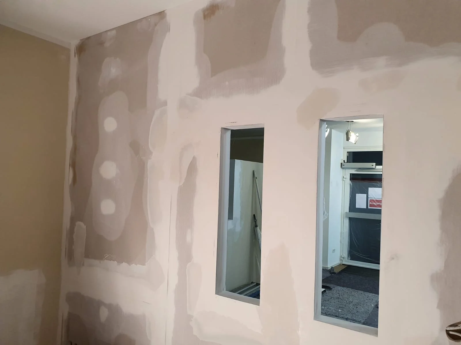 Innenwand im Renovierungsprozess mit zwei rechteckigen Aussparungen für Fenster, leicht ungleichmäßige Spachtelarbeiten sichtbar.
