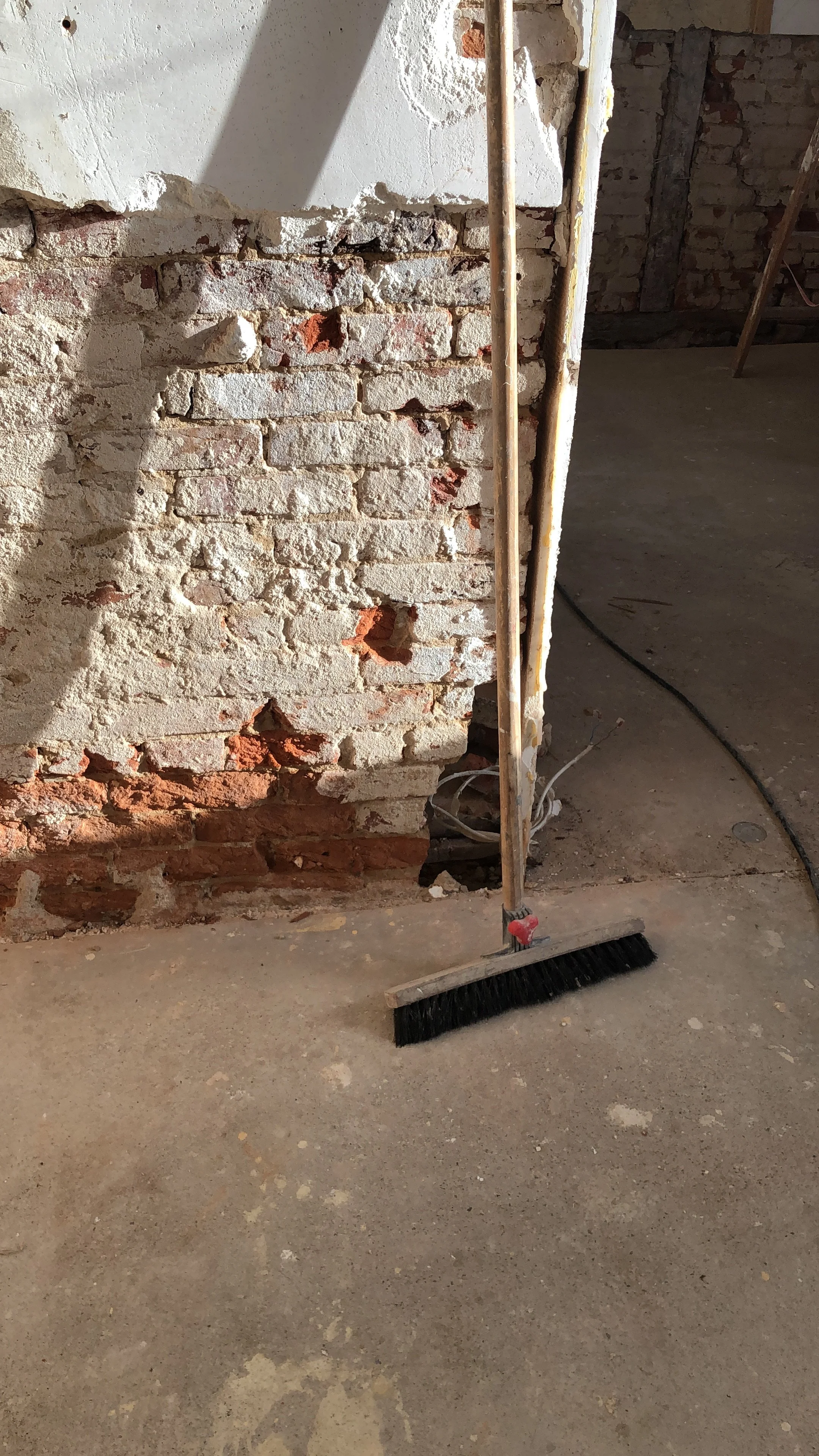 Eine Baustelle mit einer alten Backsteinmauer, einer Bürste und einem Kehrblech auf dem Boden.