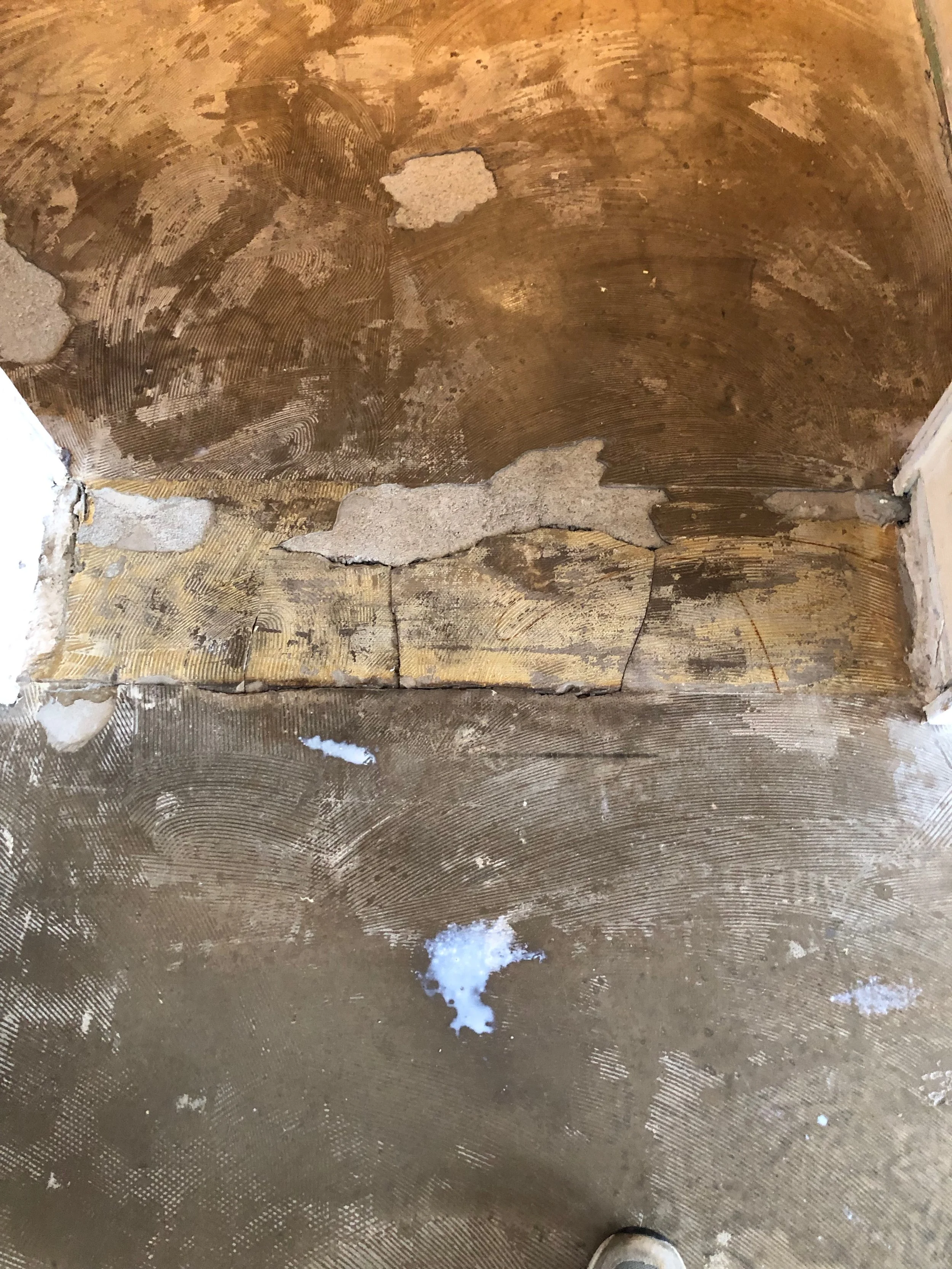 Eine zerlegte Badewanne mit freiliegendem Untergrund und noch sichtbarer künstlerischer Musterung, einige Bauschuttreste und Wasserflecken auf dem Boden.