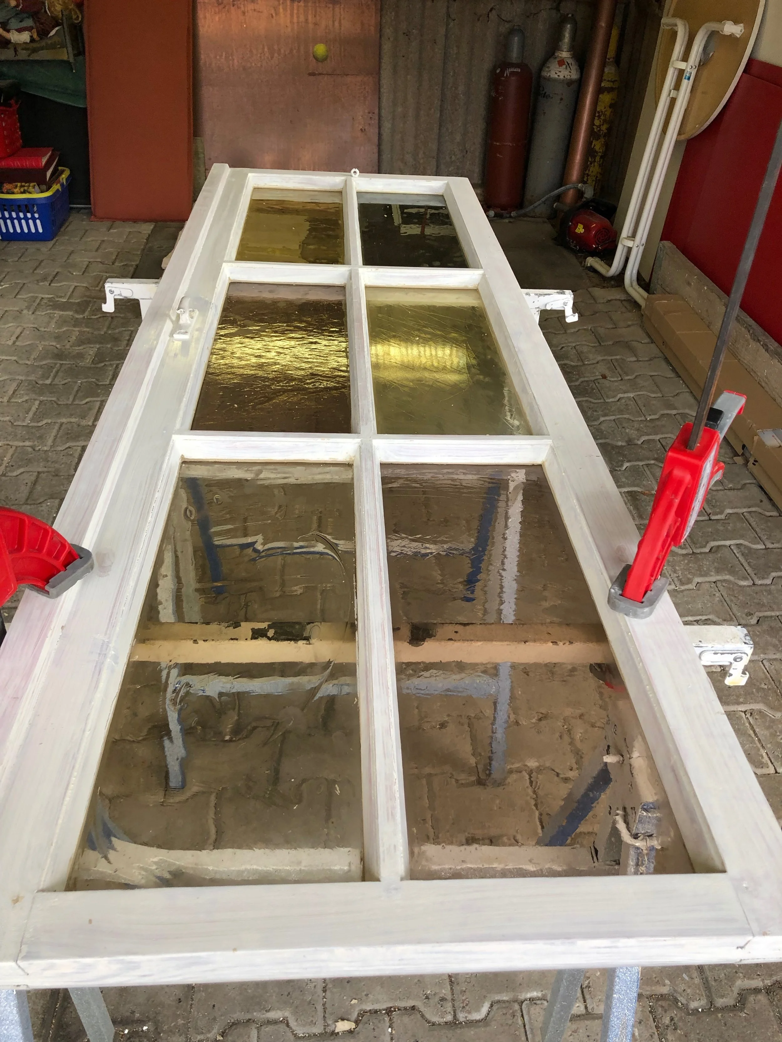 Holztür mit sechs Fenstern, die im Rahmen auf einem Arbeitstisch befestigt ist, im Werkstattumfeld.