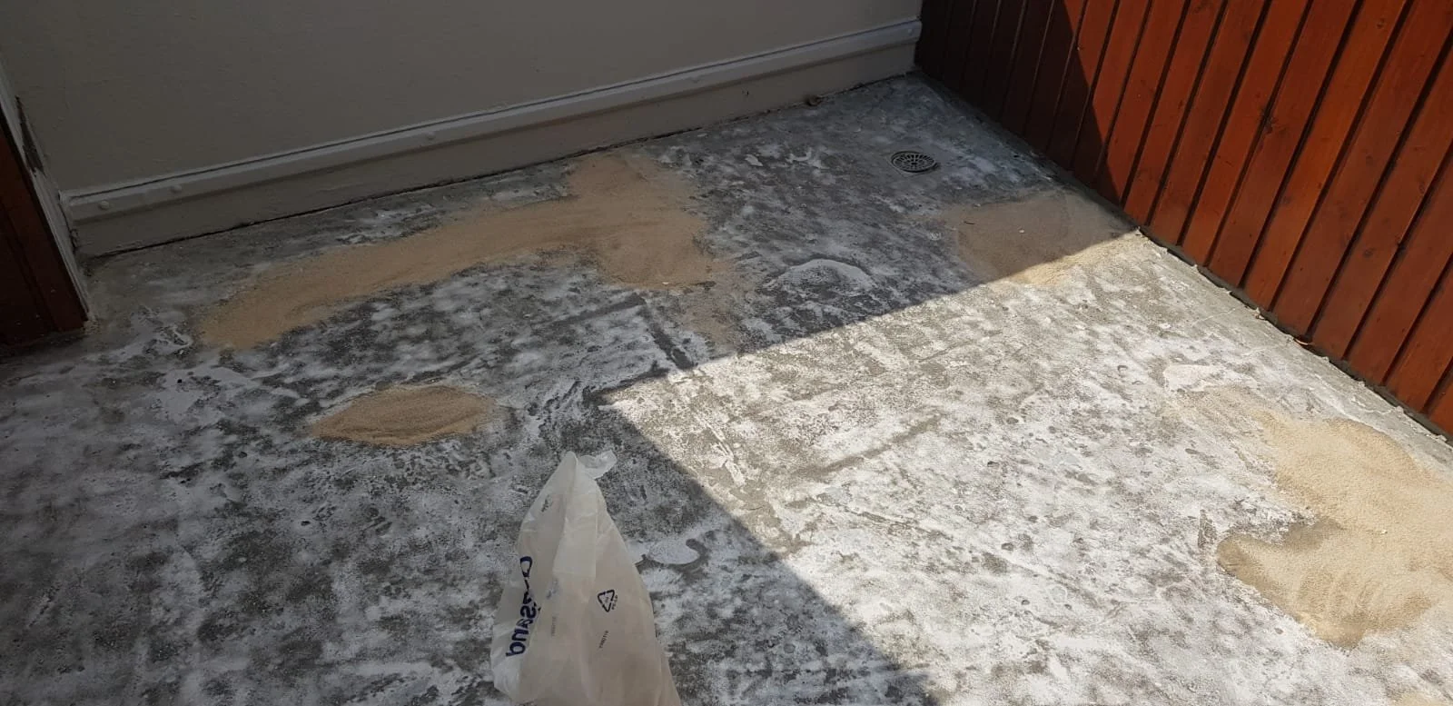 Boden mit Fliesen, teilweise mit Sand bedeckt, im Eingangsbereich mit Holzverkleidung an der Wand.